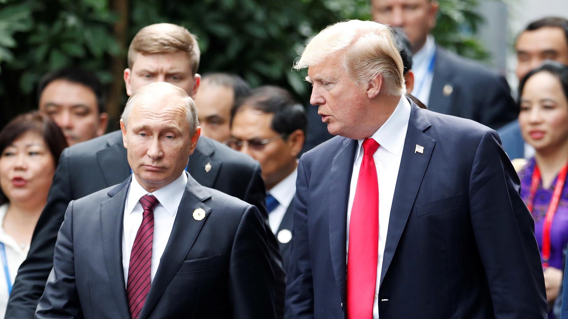 US President Donald Trump and Russian President Vladimir Putin are seen walking side-by-side surrounded by other officials.