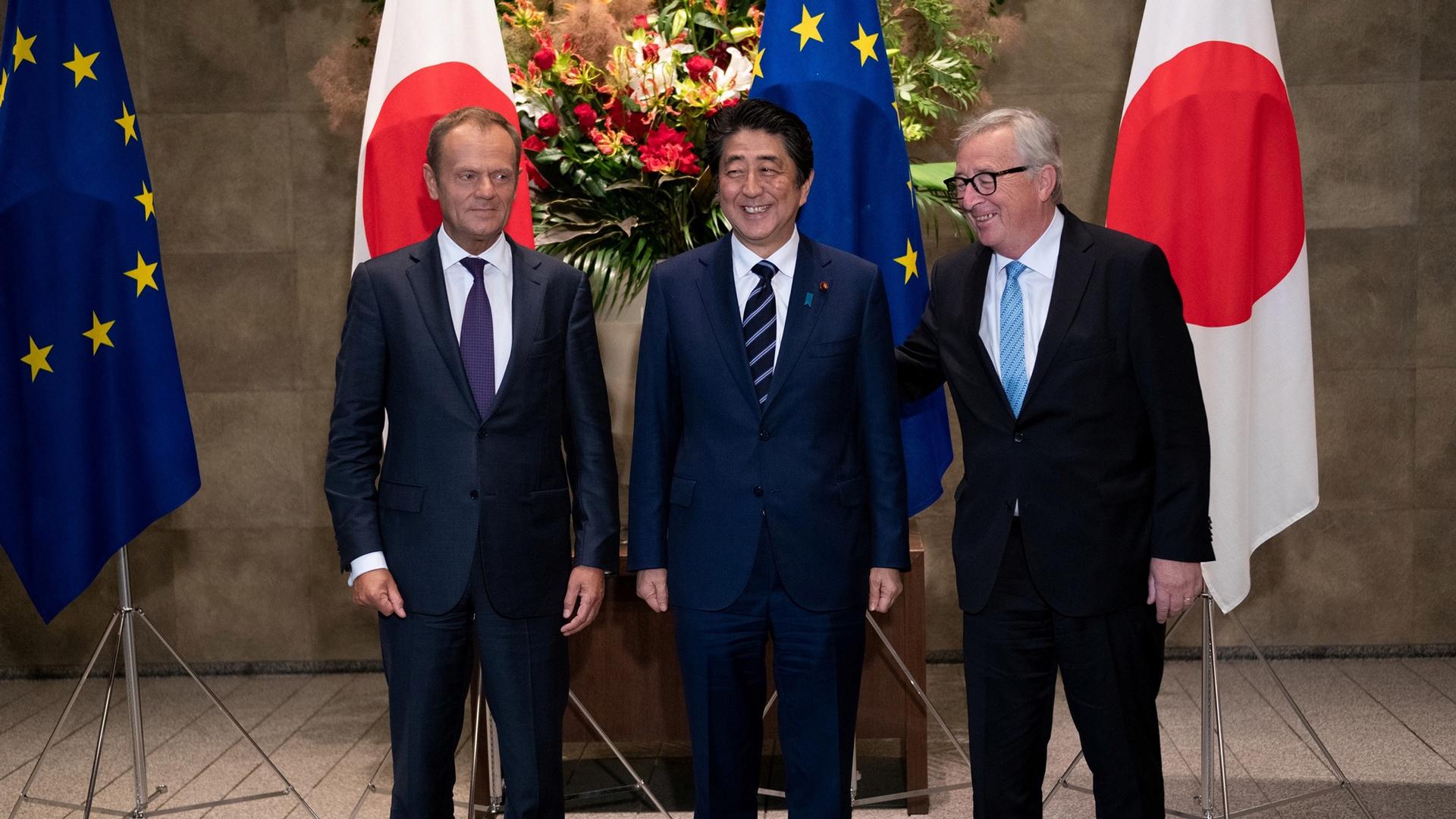 Japanese Prime Minister Shinzo Abe stands along side European Commission President Jean-Claude Juncker and European Council President Donald Tusk with EU and Japan flags behind them.