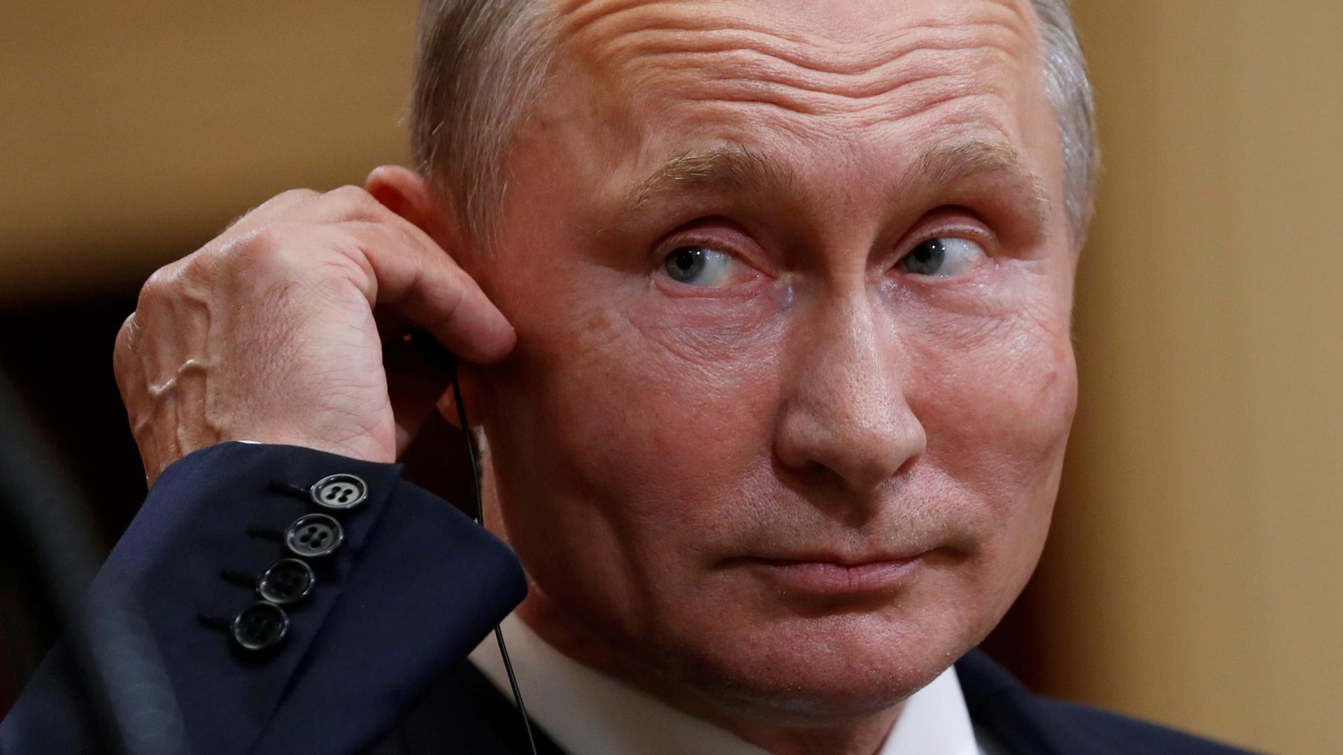 A close-up photography of Russian President Vladimir Putin touching an ear piece.
