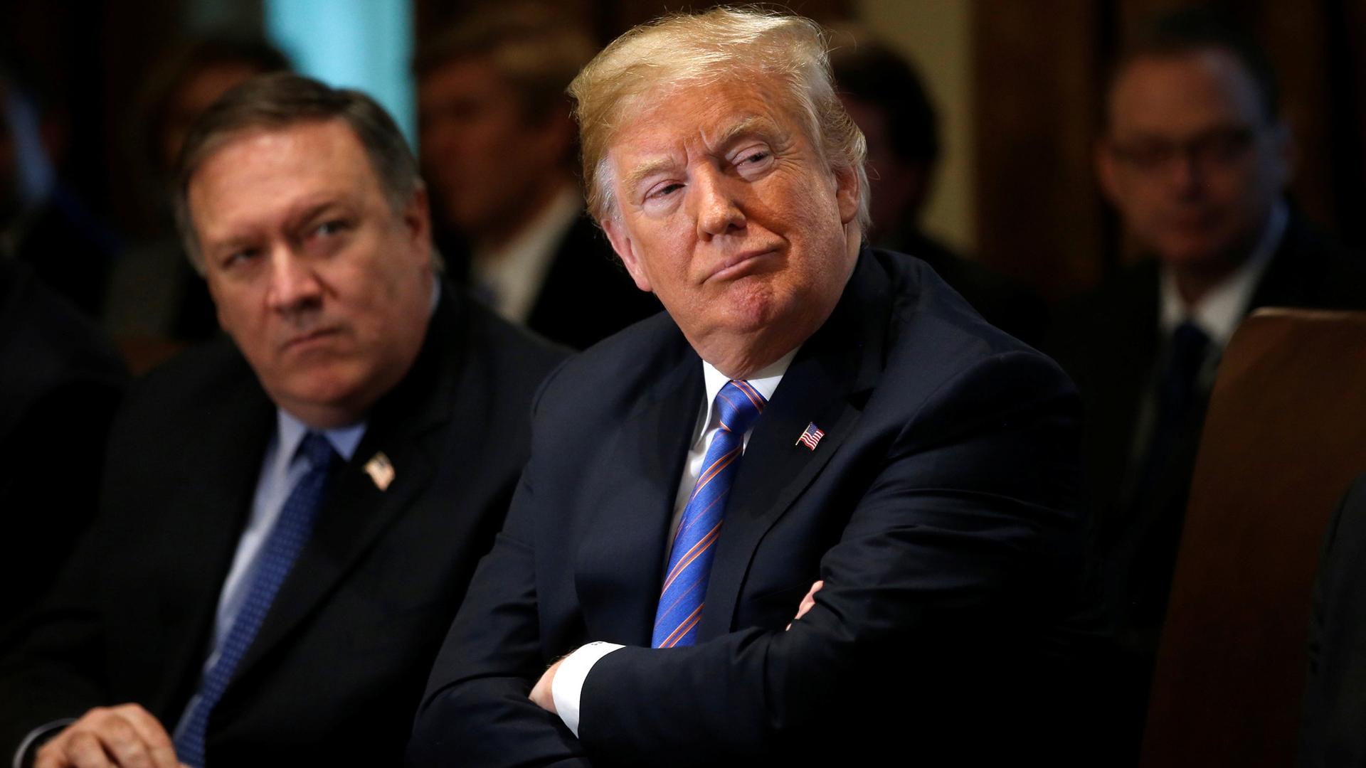 US Secretary of State Mike Pompeo is seated next to President Donald Trump who has his arms folded.