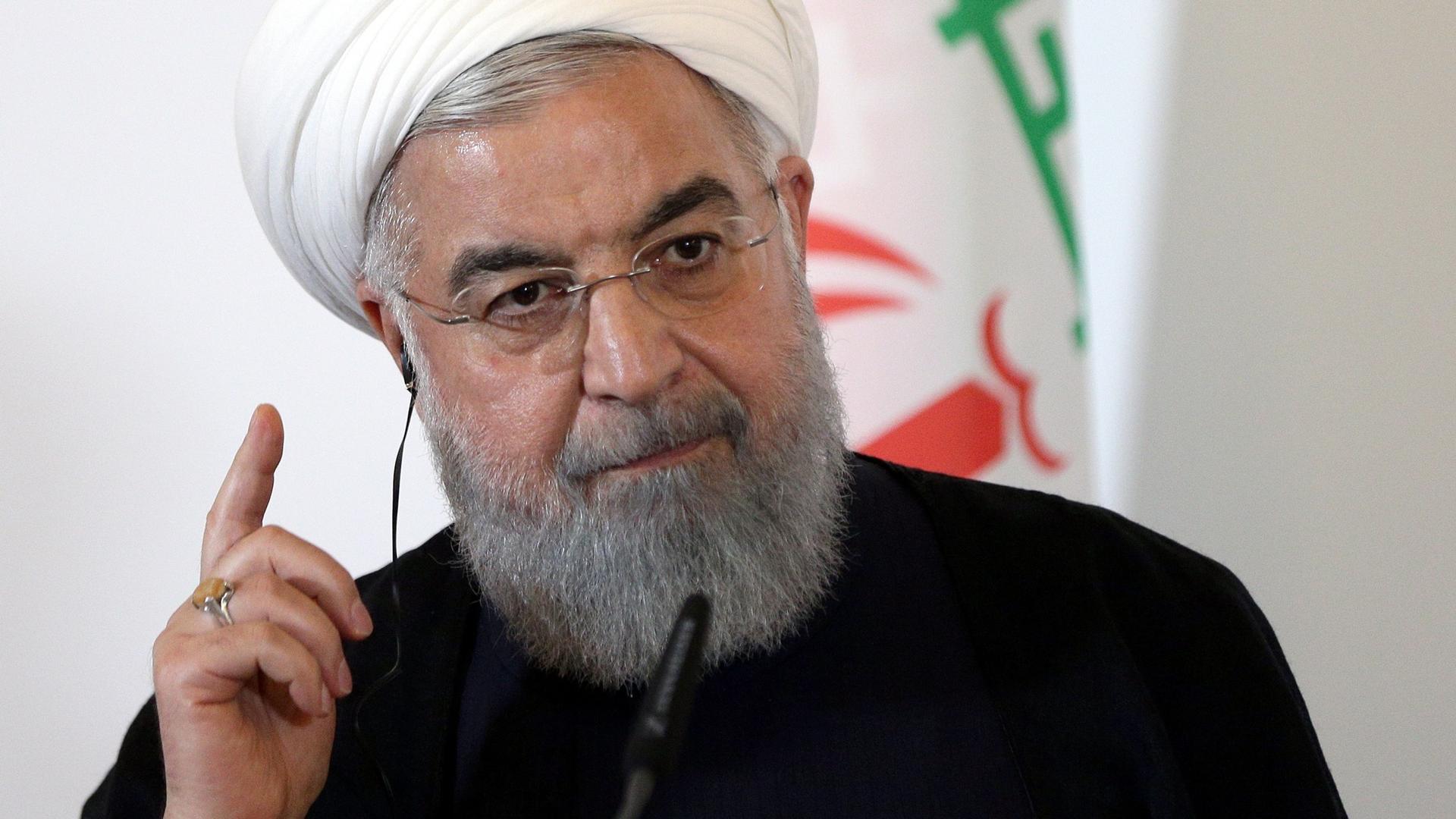 Iran President Hassan Rouhani with his right hand raised and finger pointed upward.