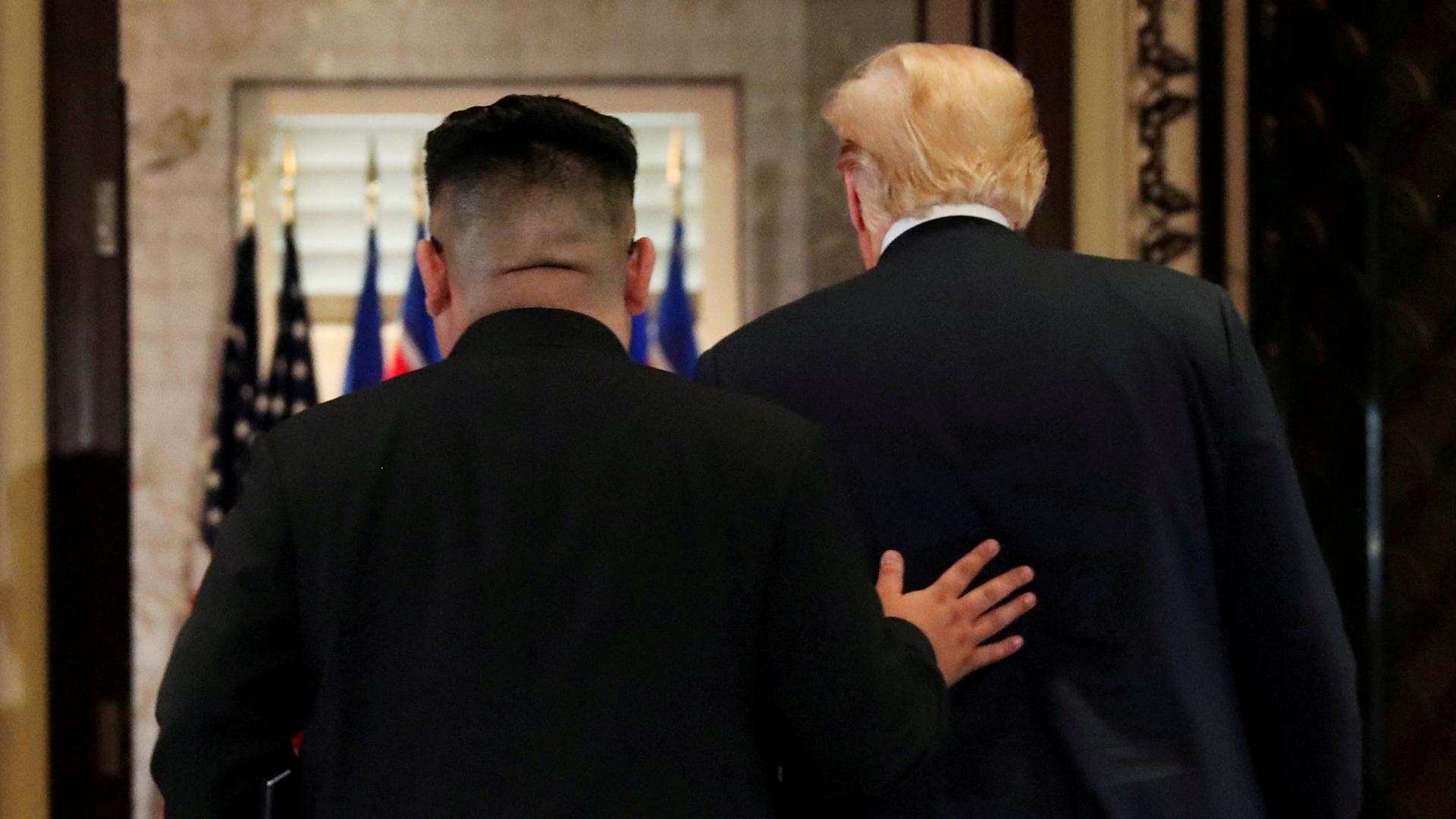 US President Donald Trump is seen walking next to North Korea's leader Kim Jong-un  who has his hand on Trump's back.