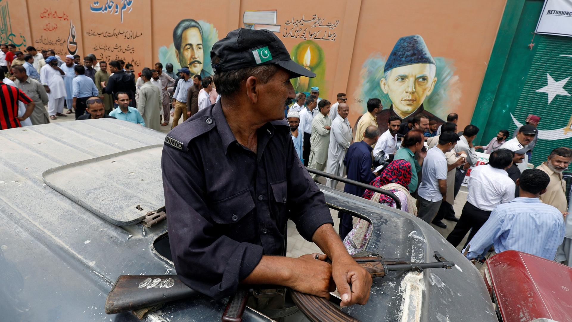 A security officer is seen perched through a vehicle's sun roof as electoral workers stand in line along a wall in Karachi, Pakistan.