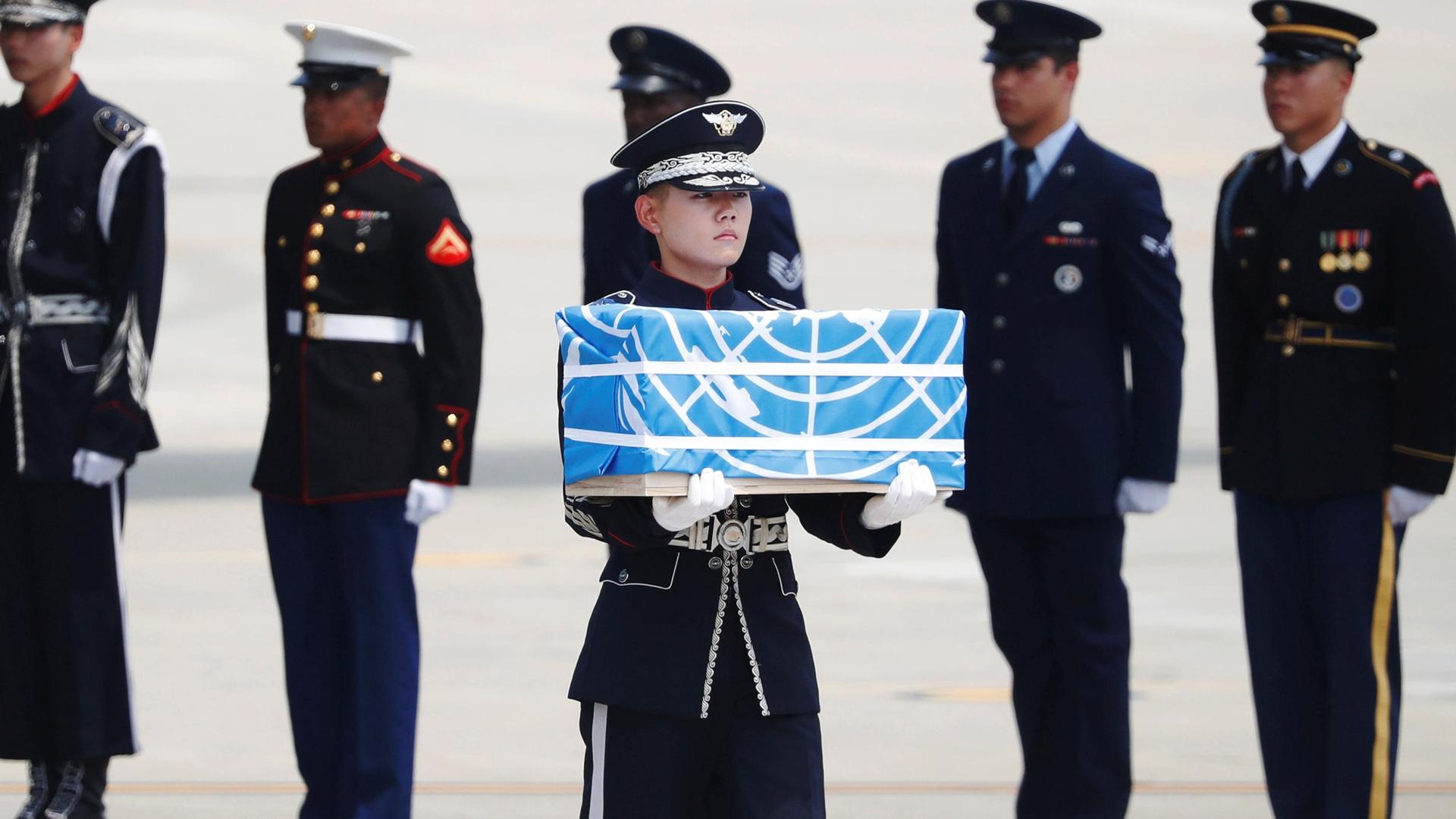 A uniformed soldier carries a casket containing the remains of a US soldier draped in a blue flag.