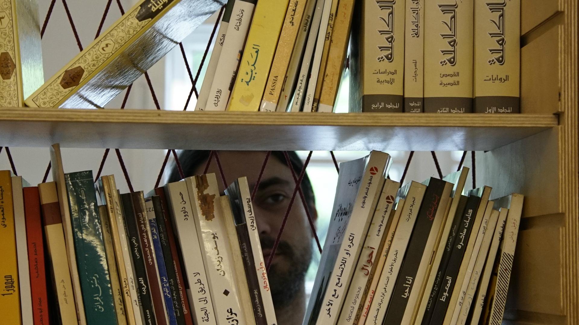 Muhanned Qaiconie, a co-founder of Berlin's first Arabic-language public library, looks at books in the collection. “All kinds of people come here,” he said. “We have older generations of Arabic speakers, new readers, seasoned bookworms, aspiring writers 