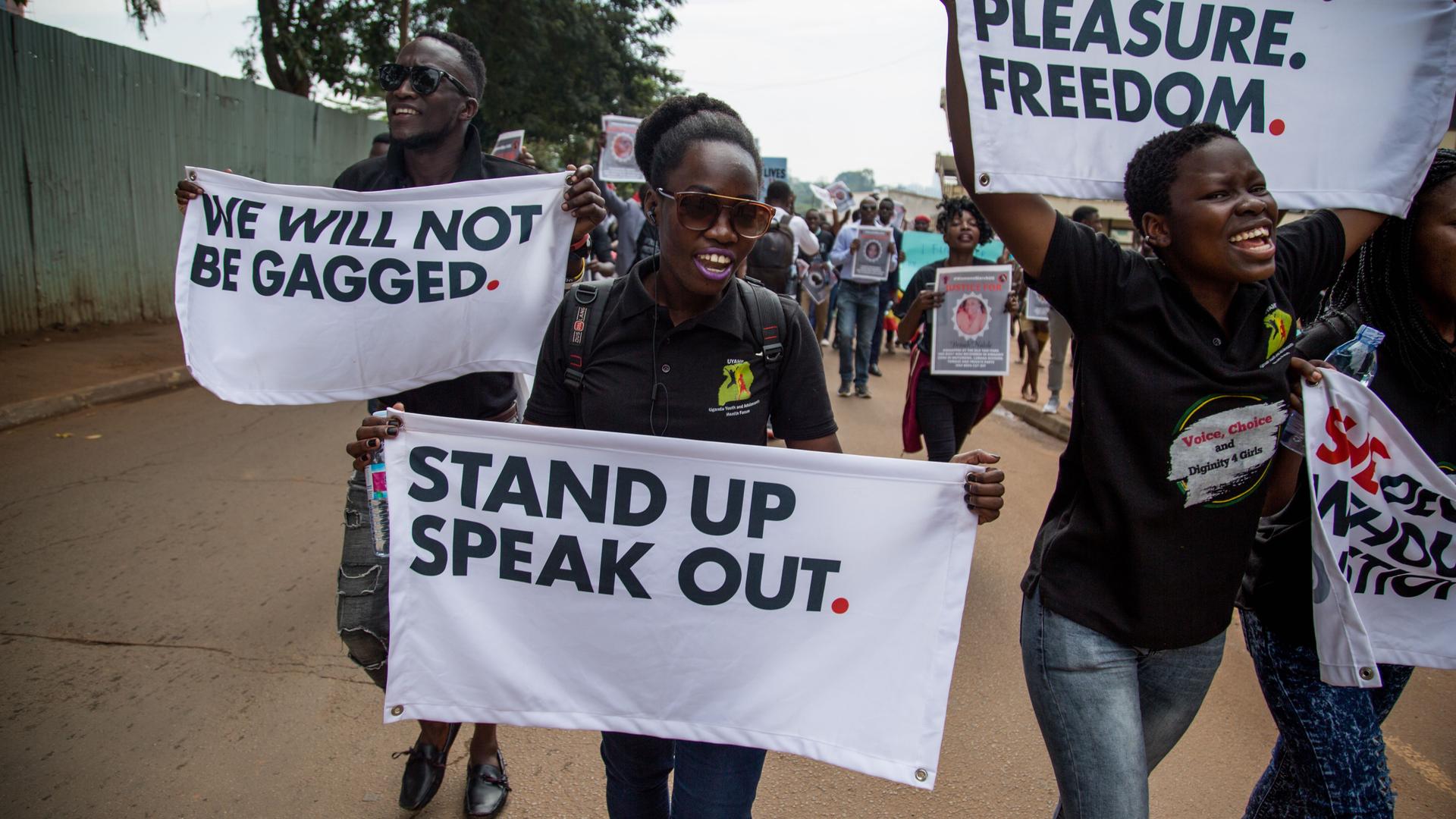 Men and women are walking in the streets of Kampala holding placards with messages in support of women's rights.