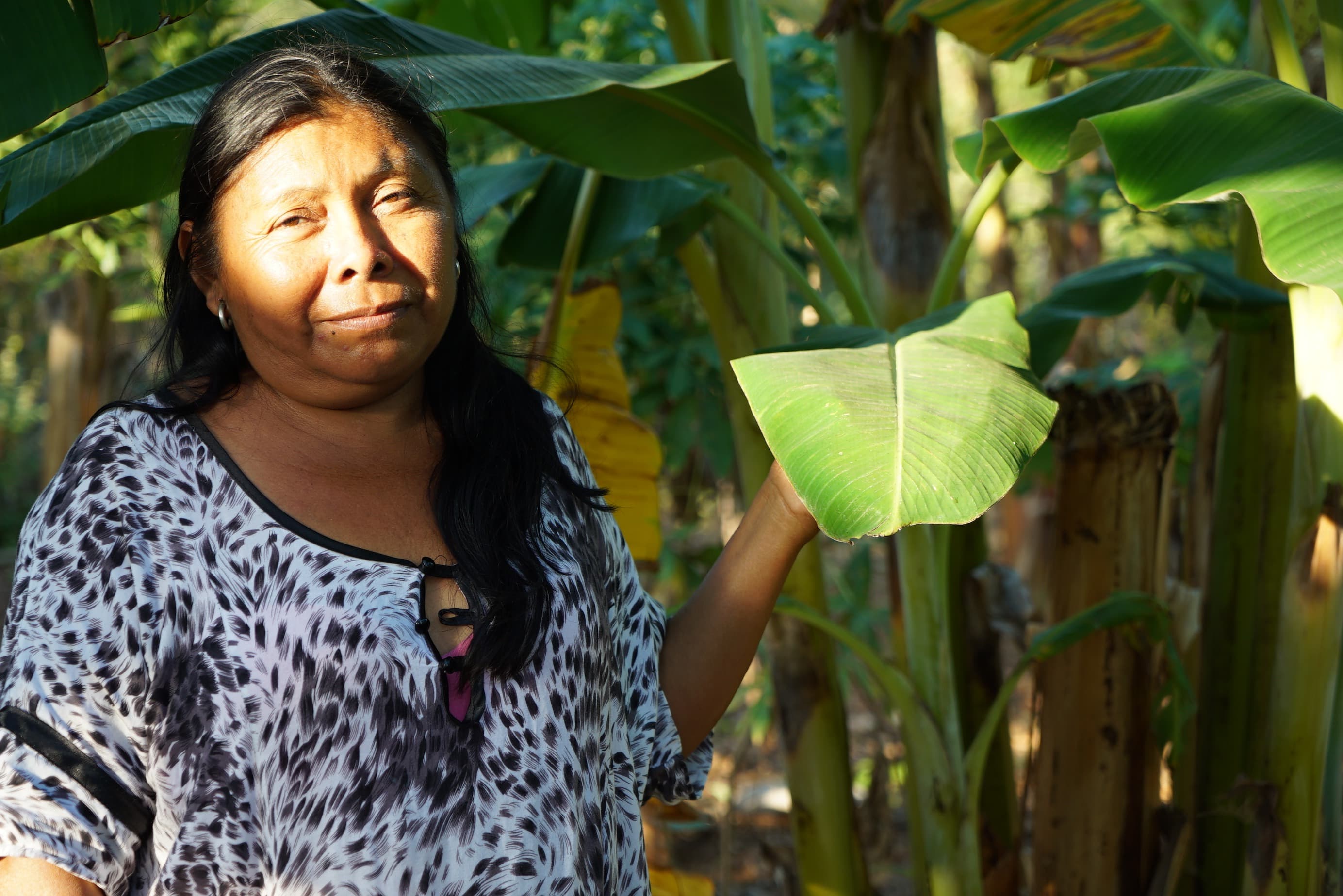 a woman with long dark hair stands by a plant