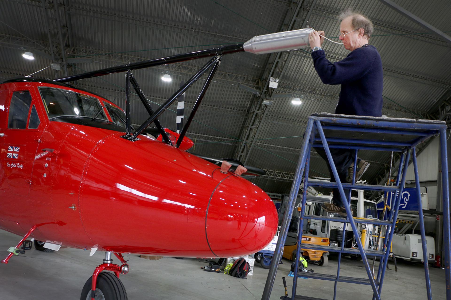A man on a ladder works on a cherry red science airplane