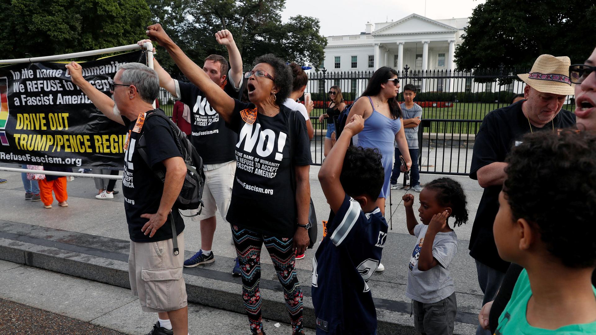 People stand in front of the White House with a sign that says "Drive out Trump-Pence regime"