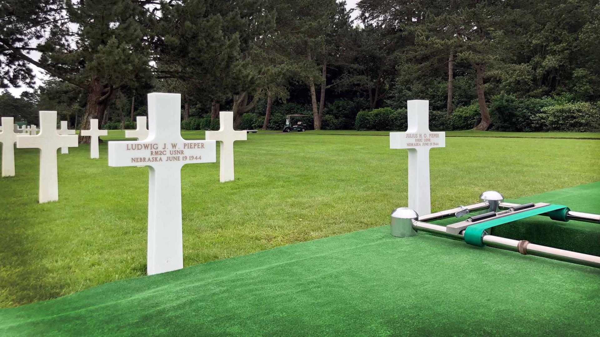 Two white crosses engraved with names sit in a cemetary