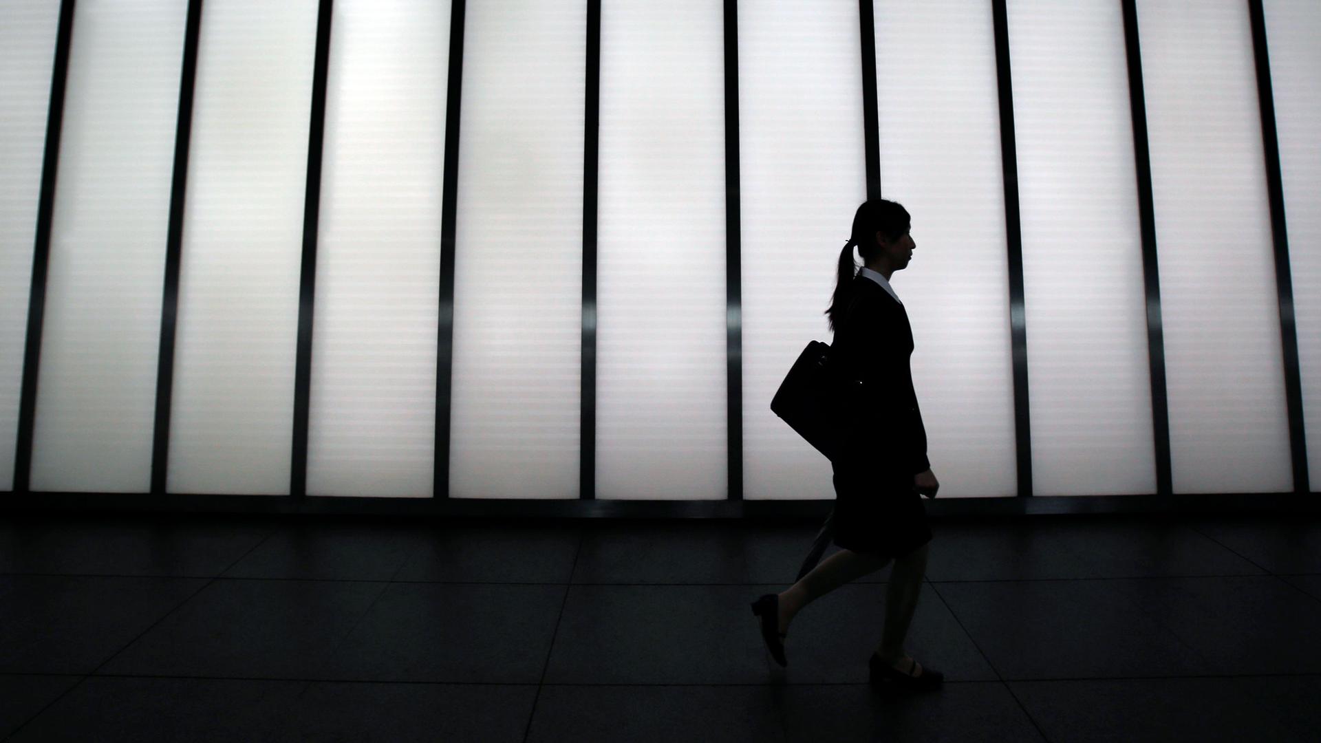 A woman in a business suit is silhouetted against a bright building