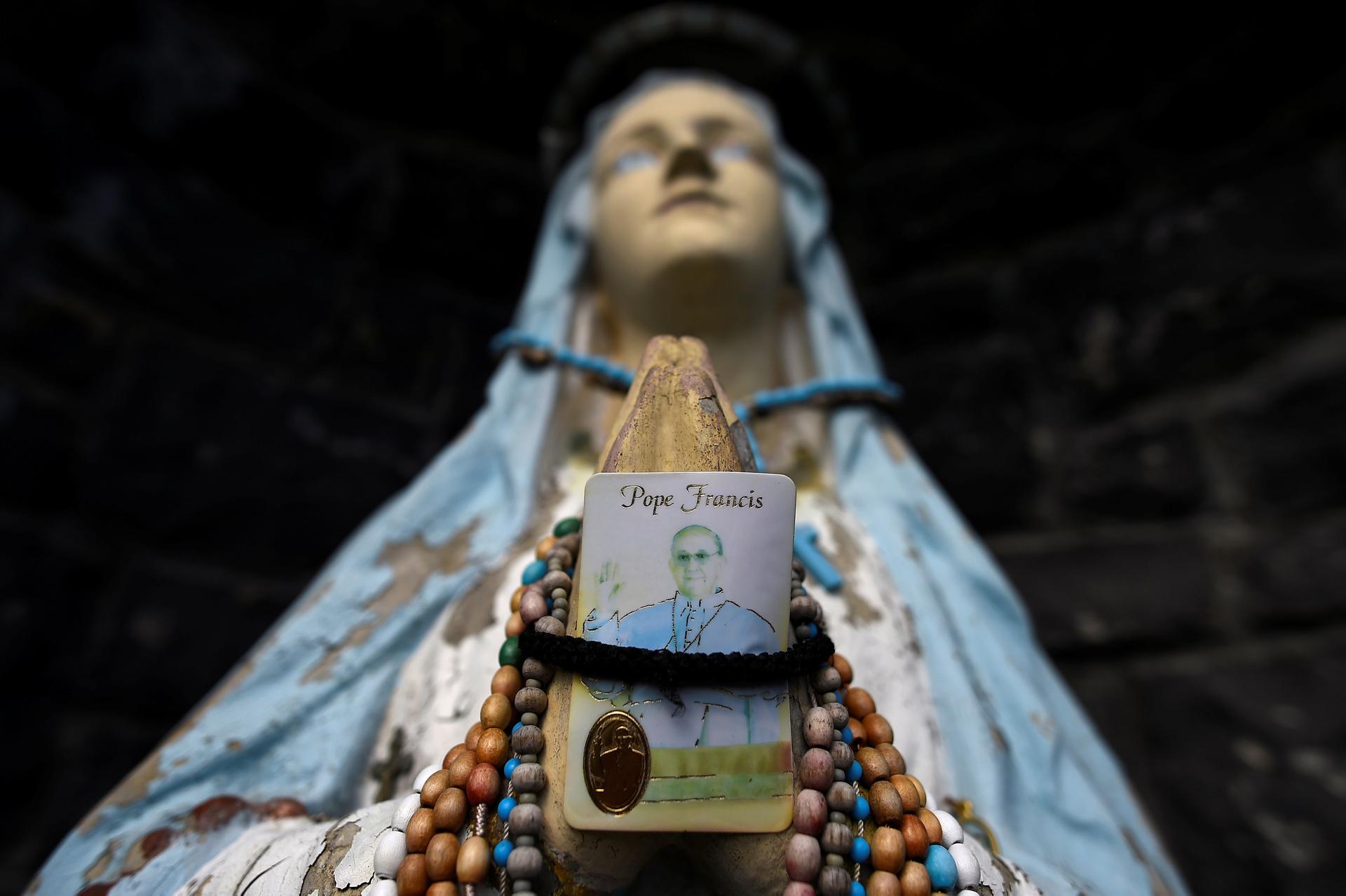 A religious grotto featuring a statue of the Virgin Mary holding a Pope Francis prayer card