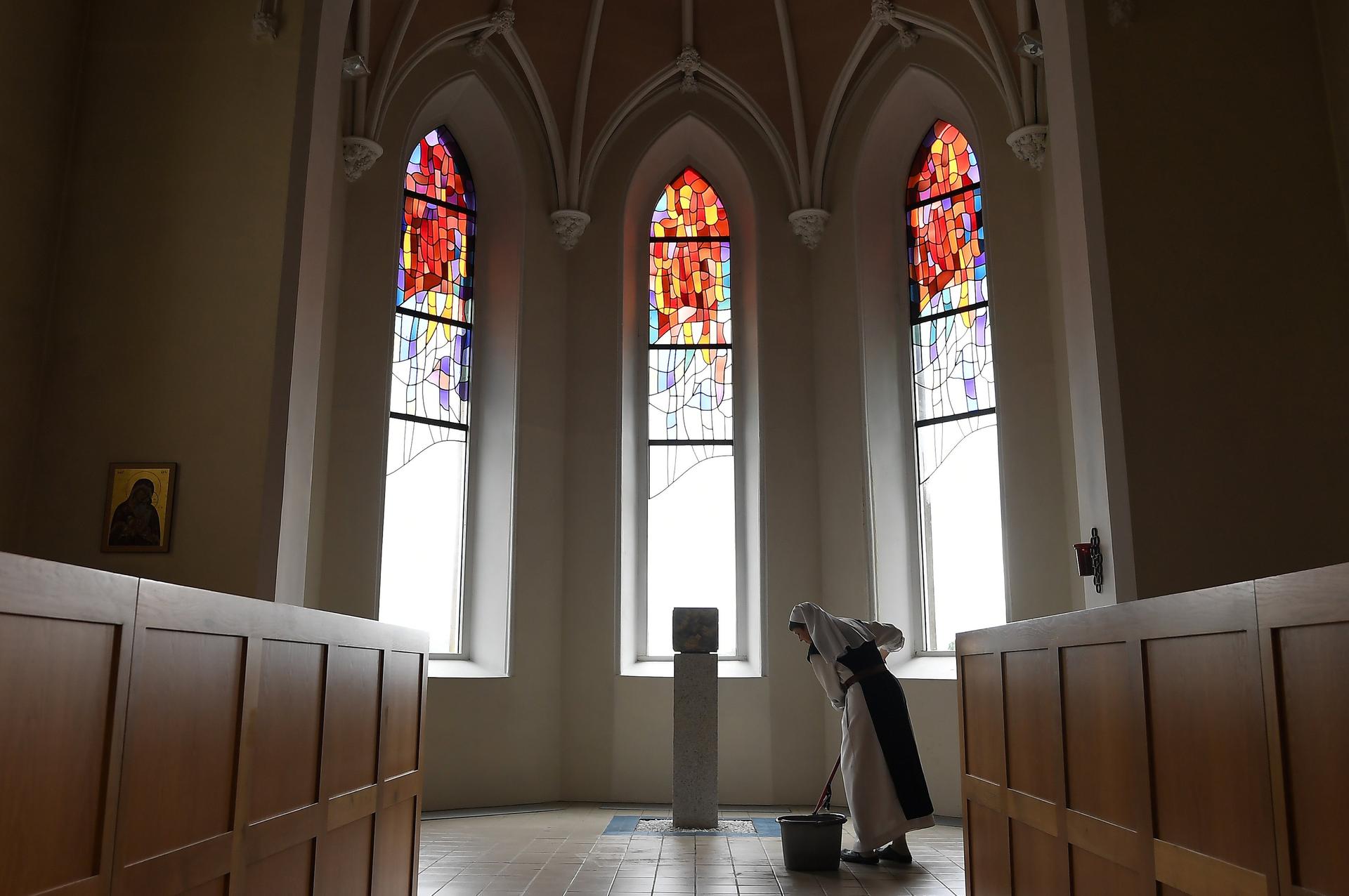 a nun in white, wiping the floors in front of a stained glass window