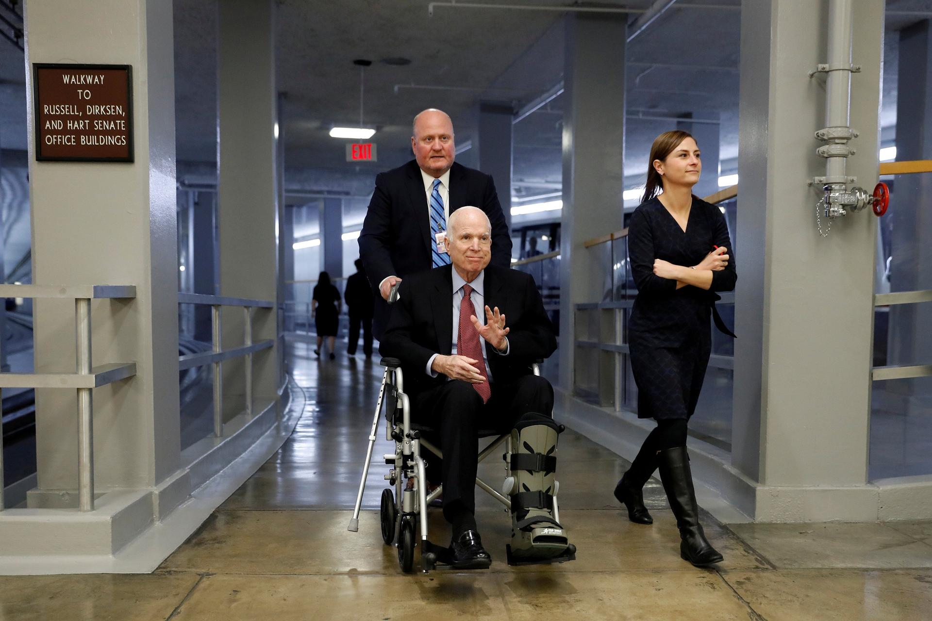 Senator John McCain sitting in a wheelchair, smiling and waving