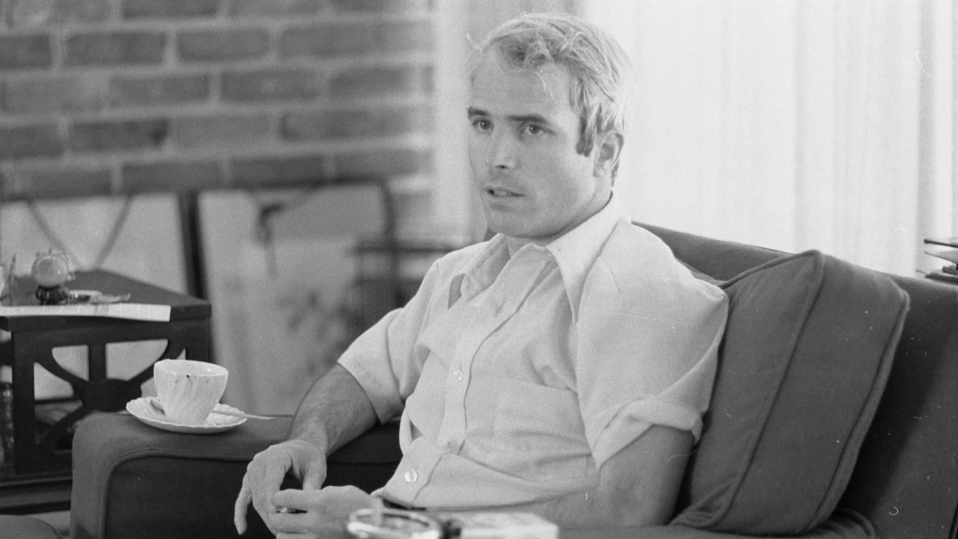 John McCain is shown in a blakc and white photographer in 1973, being interviewed about his experiences as a prisoner of war during the war in Vietnam.