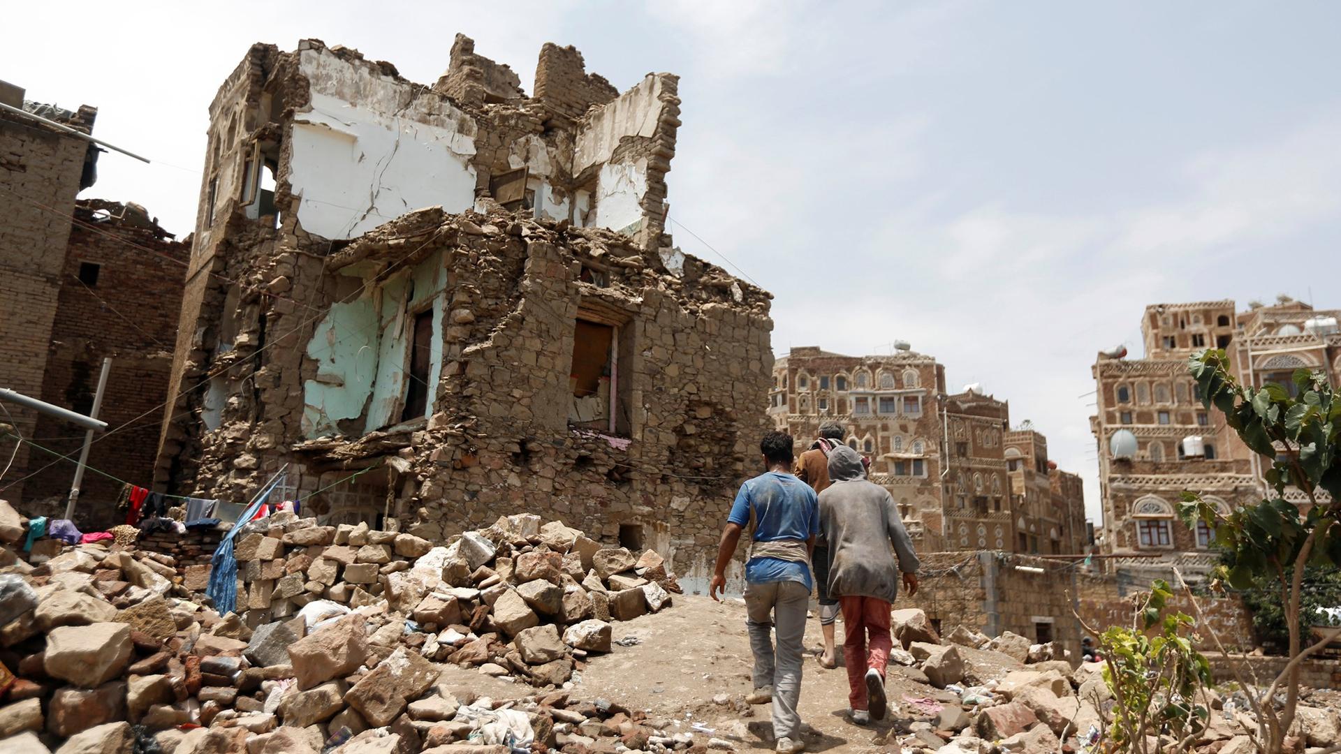 Three people walk past a stone house bombed out by an air strike in the old quarter of Sanaa, Yemen, August 8, 2018. 