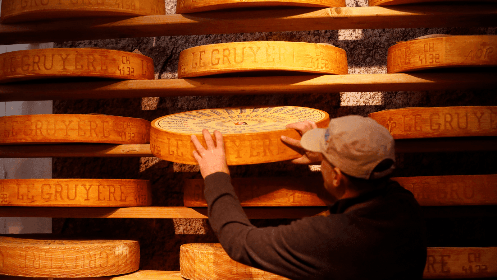 a man stands in front of a wall full of wheels of cheese