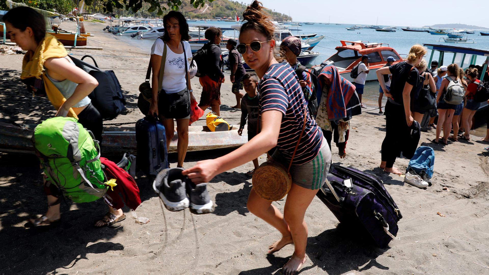 Foreign tourists carry their backpacks and rollaboards across the sandy beach after an earthquake hit Lombok island in Indonesia August 6, 2018.