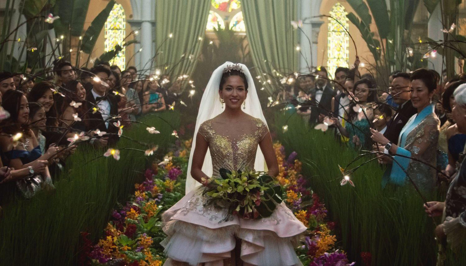 Woman in elaborate wedding dress waking down aisle, greenery, people looking on