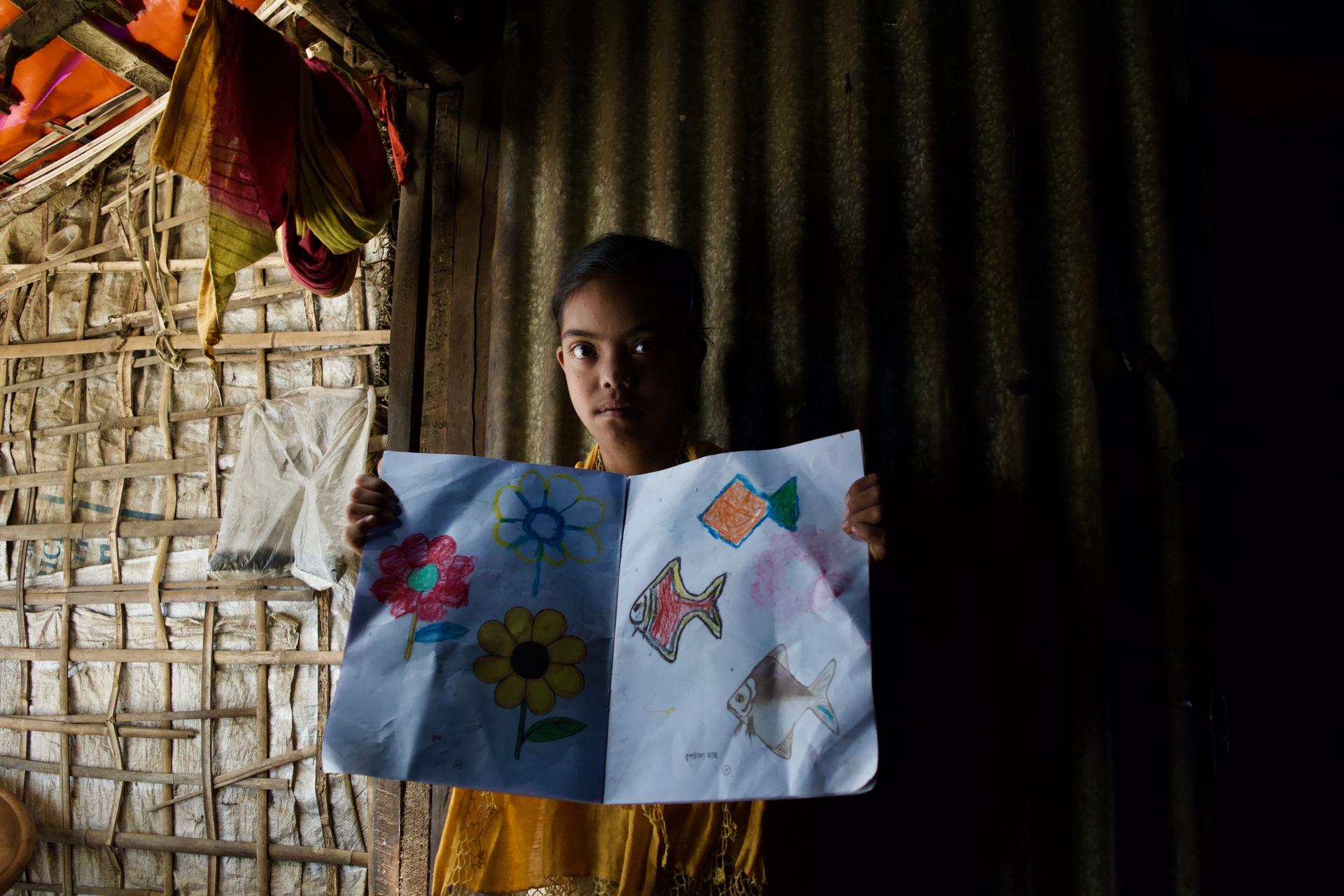 a young rohingya girl shows off a drawing