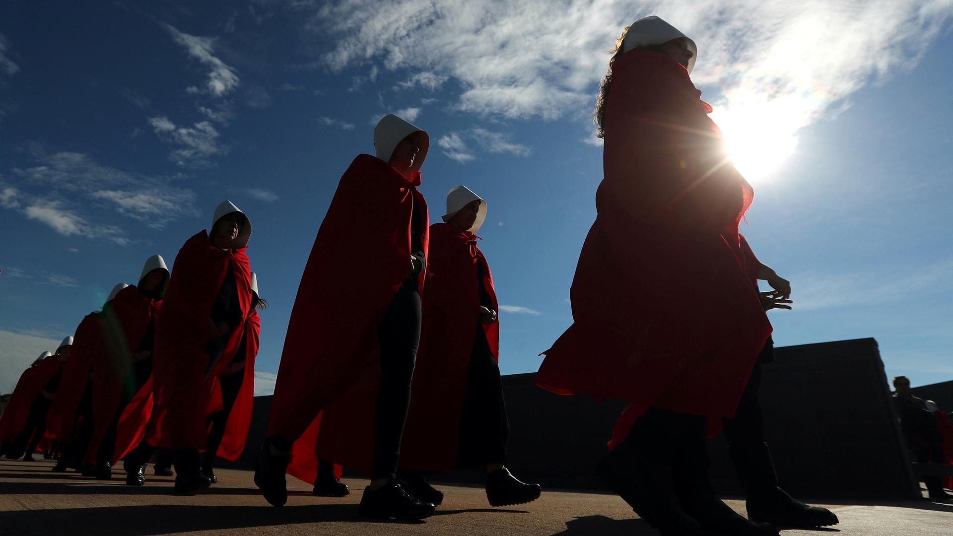 Activists dressed up as characters from "The Handmaid's Tale" are shown back lit from a low perspective.