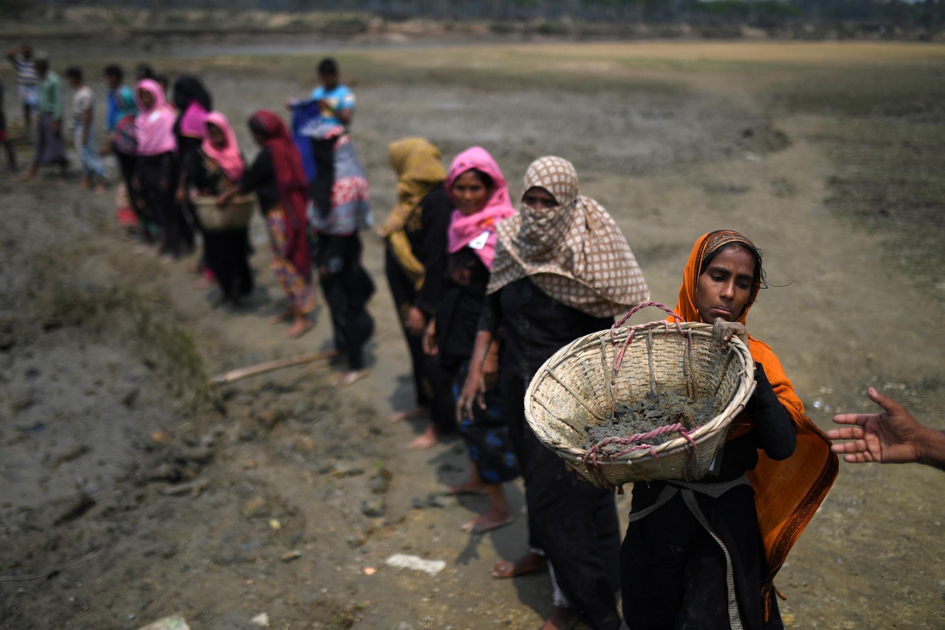 rohingya women lined up, carrying large baskets 