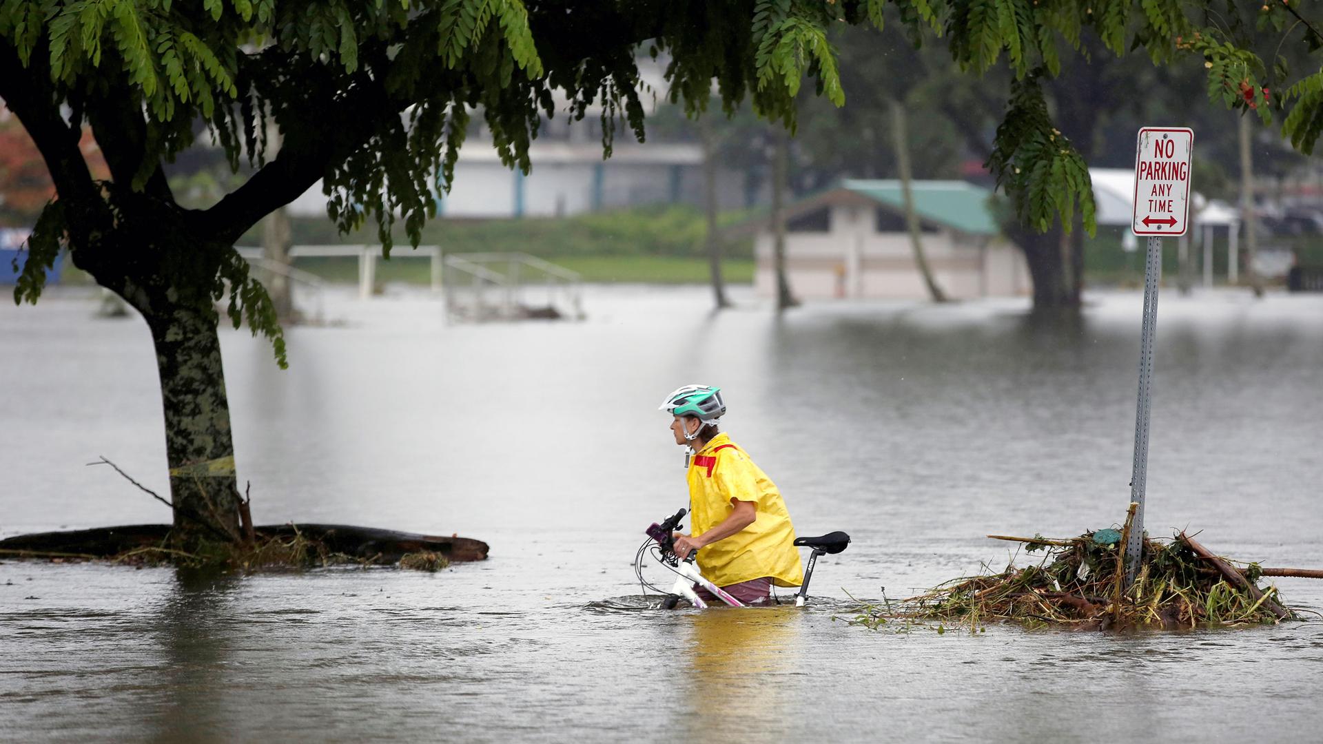 A woman rolls a bicycle through waist-high floodwaters