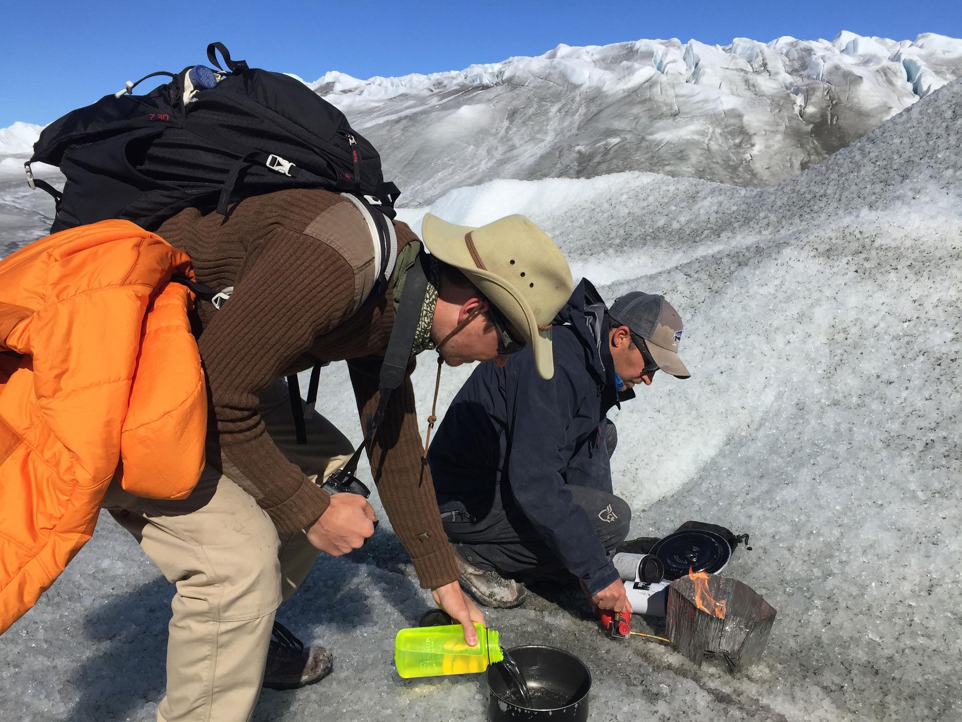 One man pours water into a pot and another starts a fire atop dirty snow