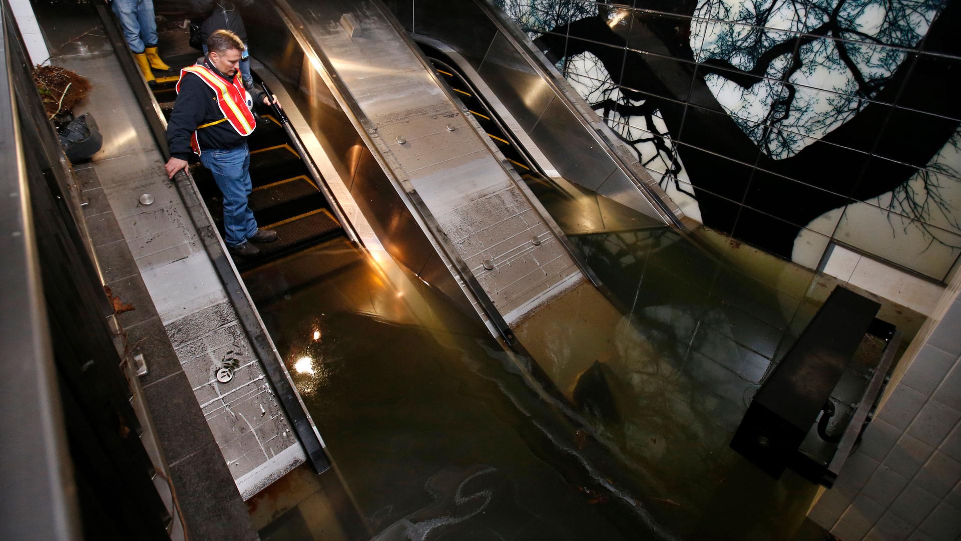 A man stands on an escalator looking down into a flooded subway station