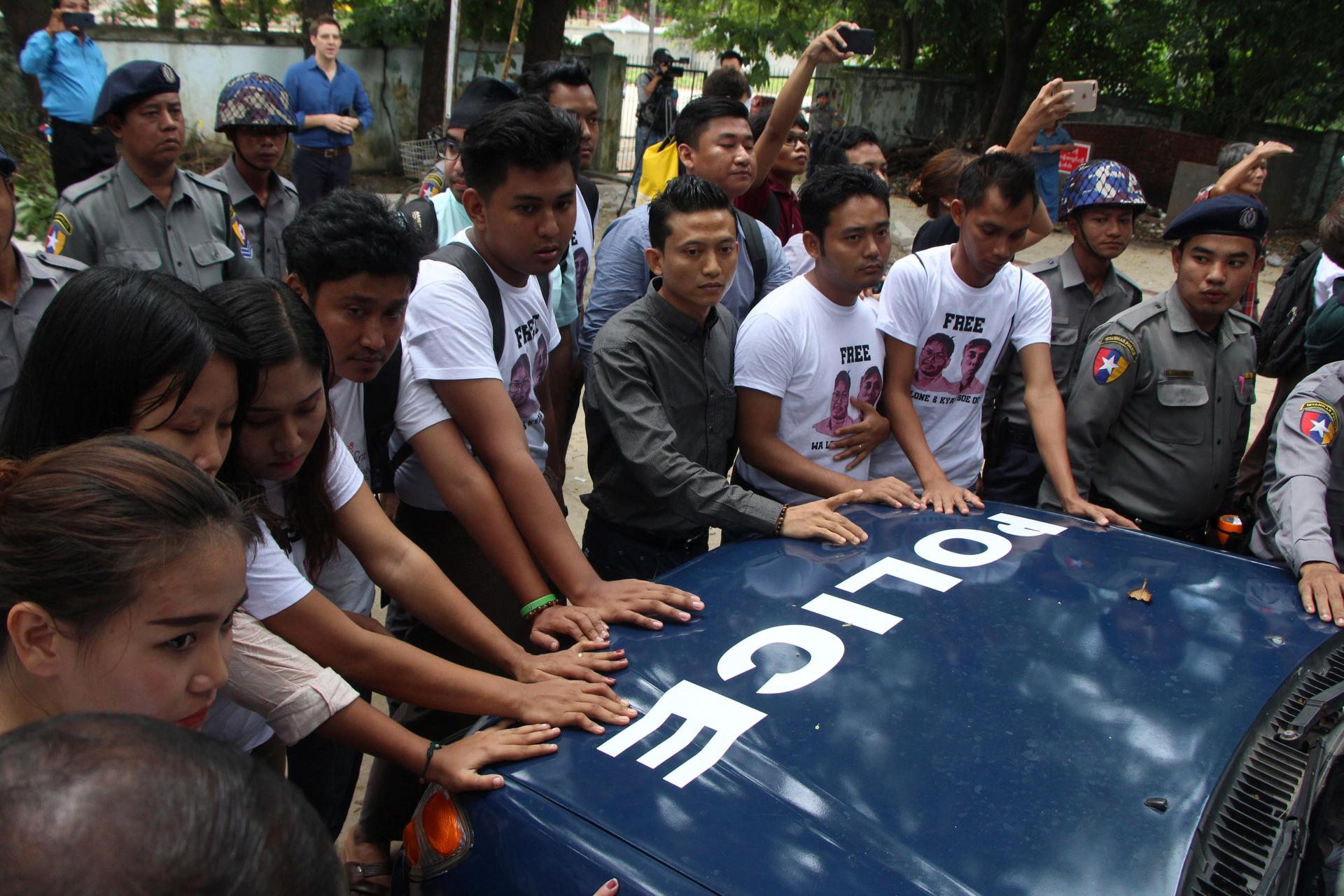 Myanmar journalists stand in front of a police vehicle