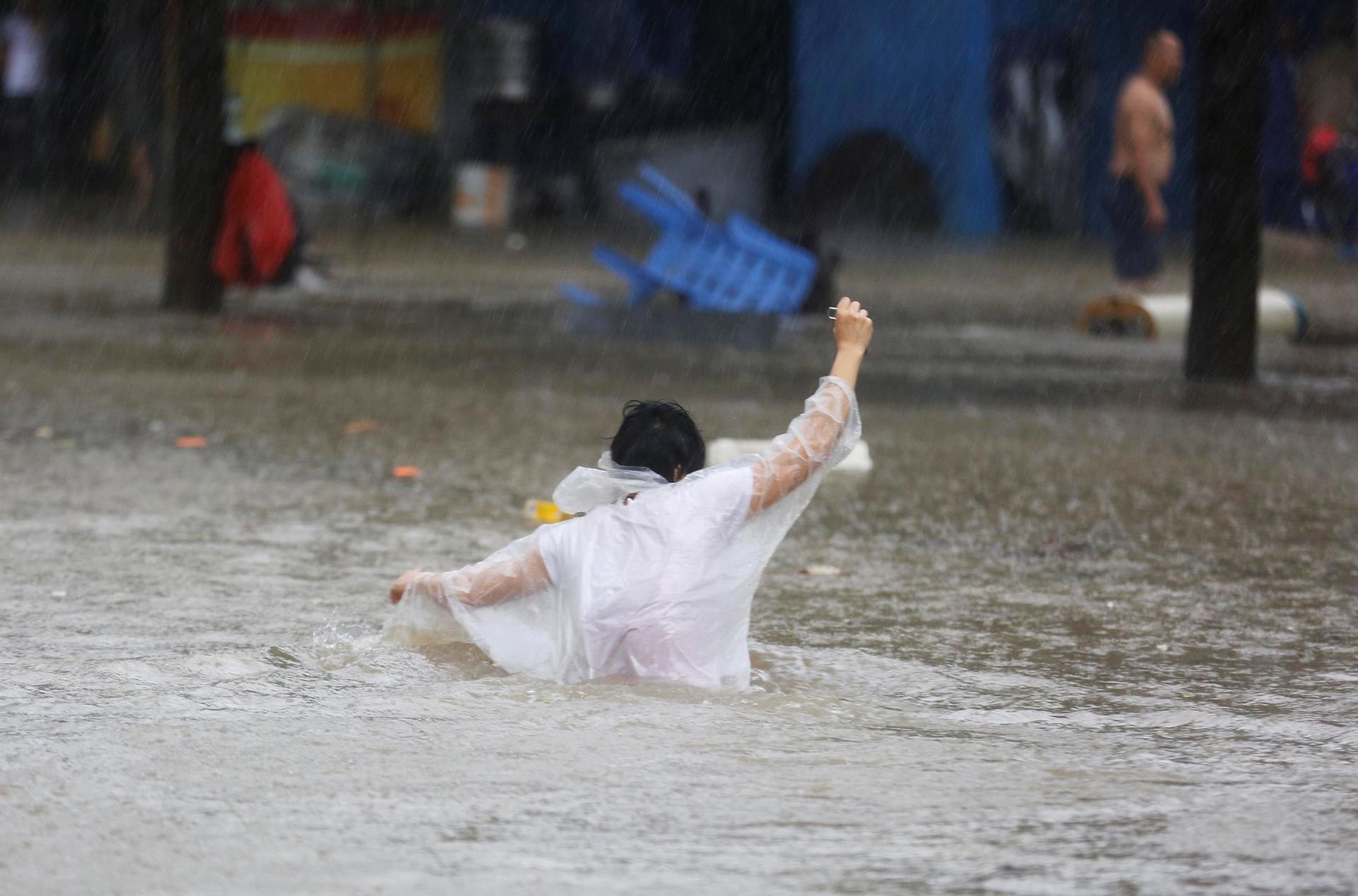A pedestrian wades through waist-high floodwaters in a white poncho