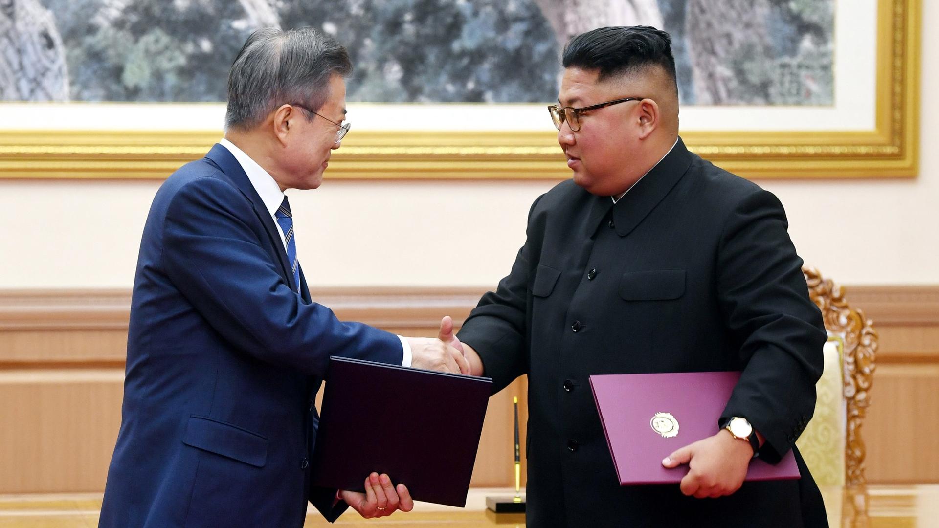 South Korean President Moon Jae-in shakes hands with North Korean leader Kim Jong-un with both carrying folders.