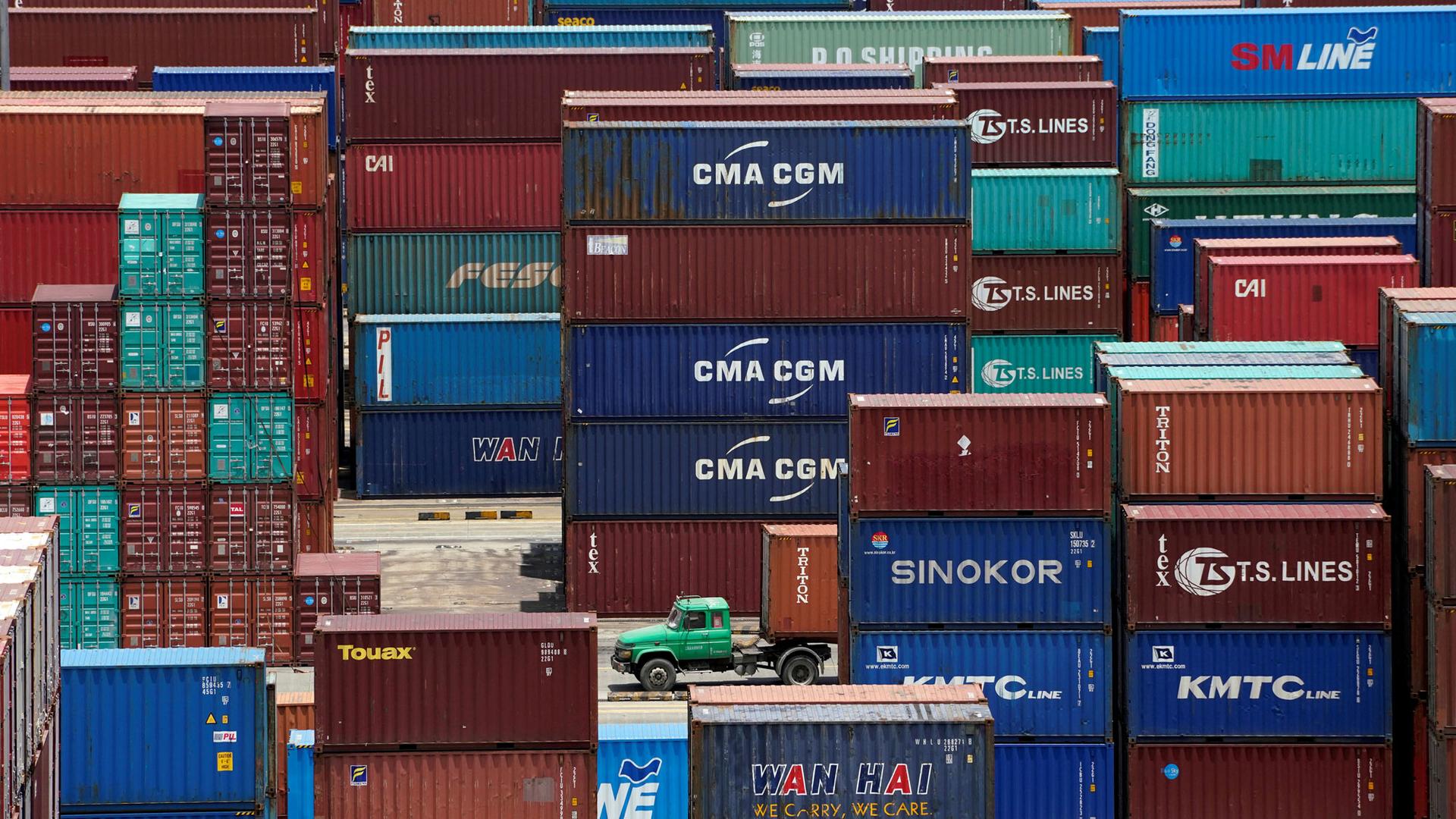 Shipping containers are seen at a port in Shanghai, China, with a green truck driving through the middle.