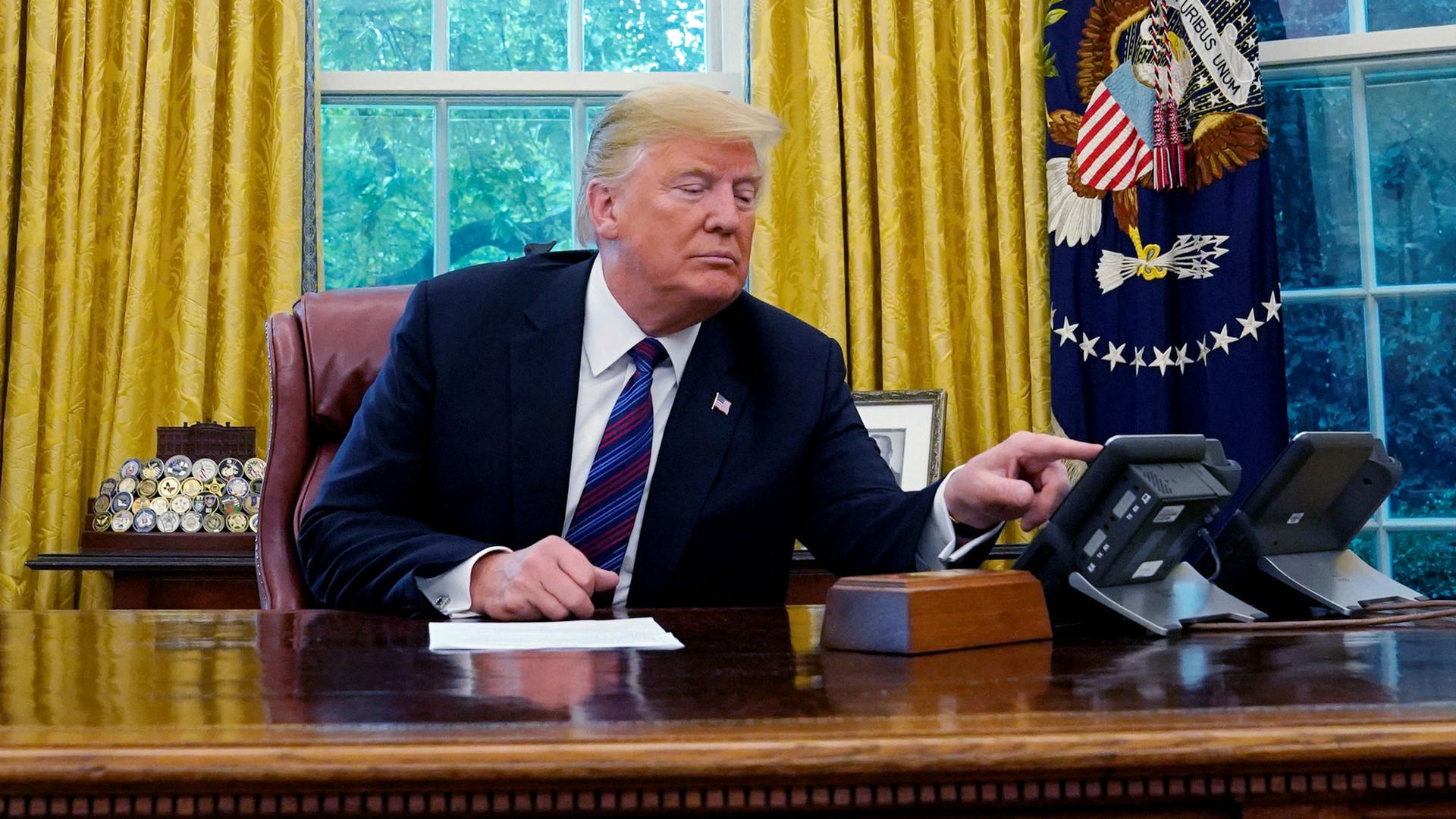 President Donald Trump is shown at his desk in the oval office talking via speakerphone.