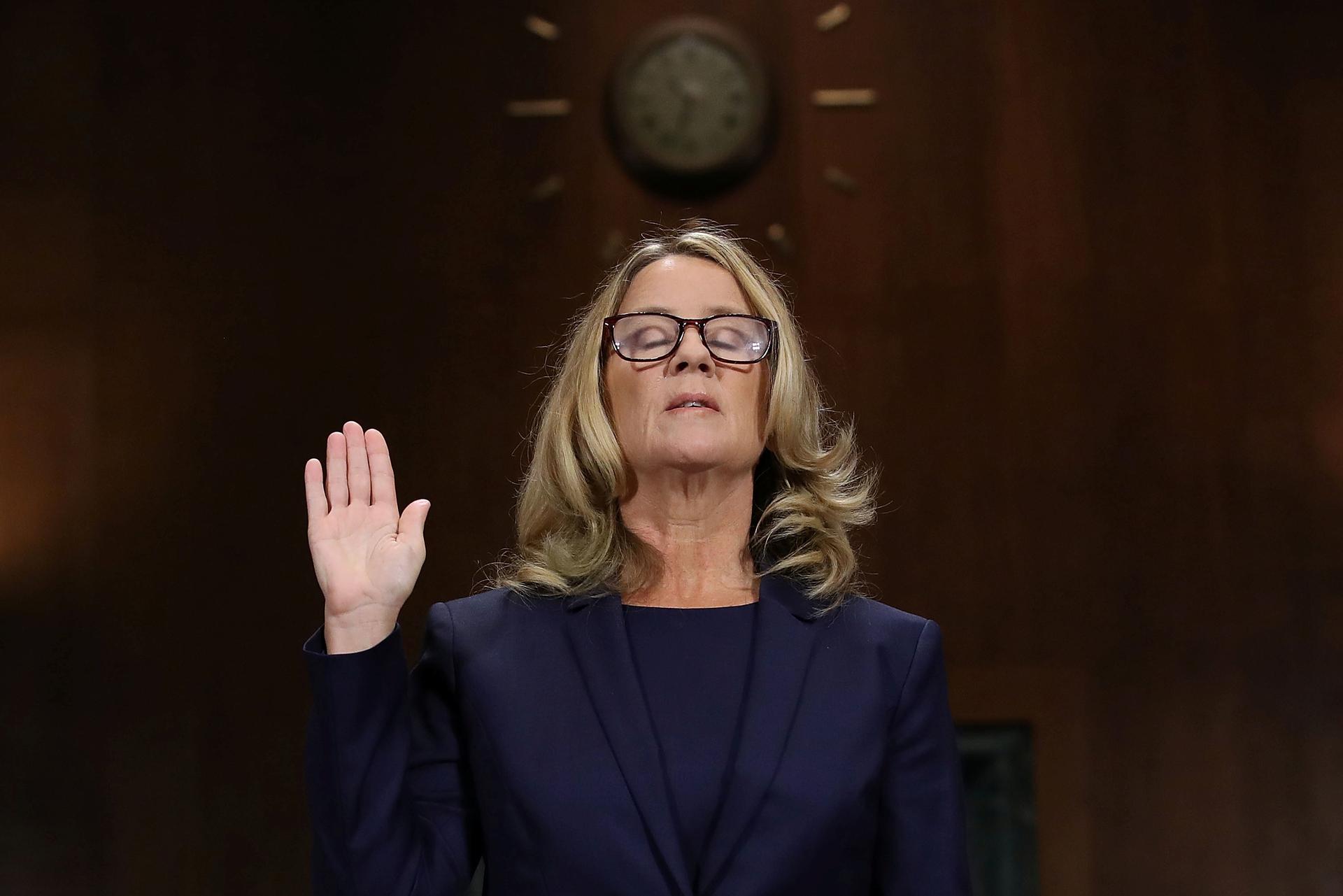 Dr. Christine Blasey Ford is shown with her right hand raised and eyes closed.