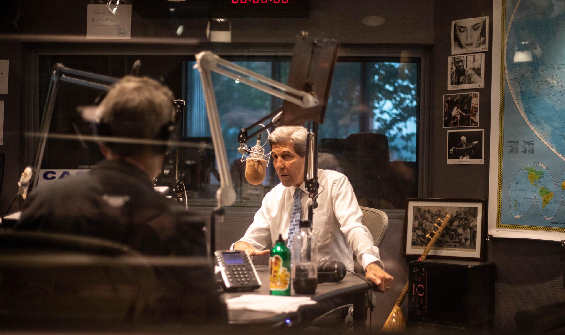 John Kerry stands behind the mic in The World studio