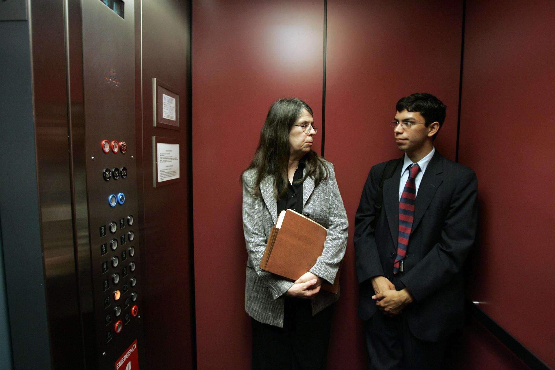 Woman and young man in suit holding papers look at each other in elevator