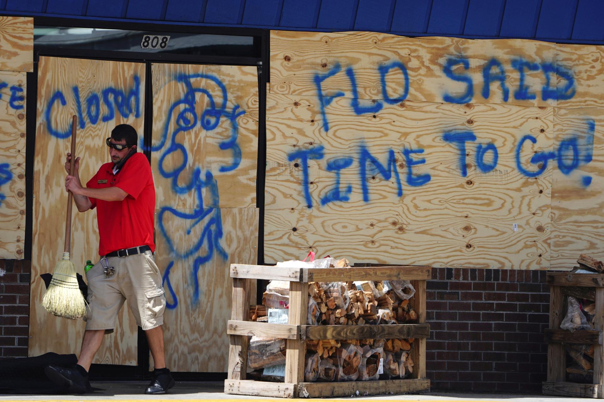 A man sweeps the entrance of a boarded up store before Hurricane Florence comes ashore in Carolina Beach, North Carolina, Wednesday