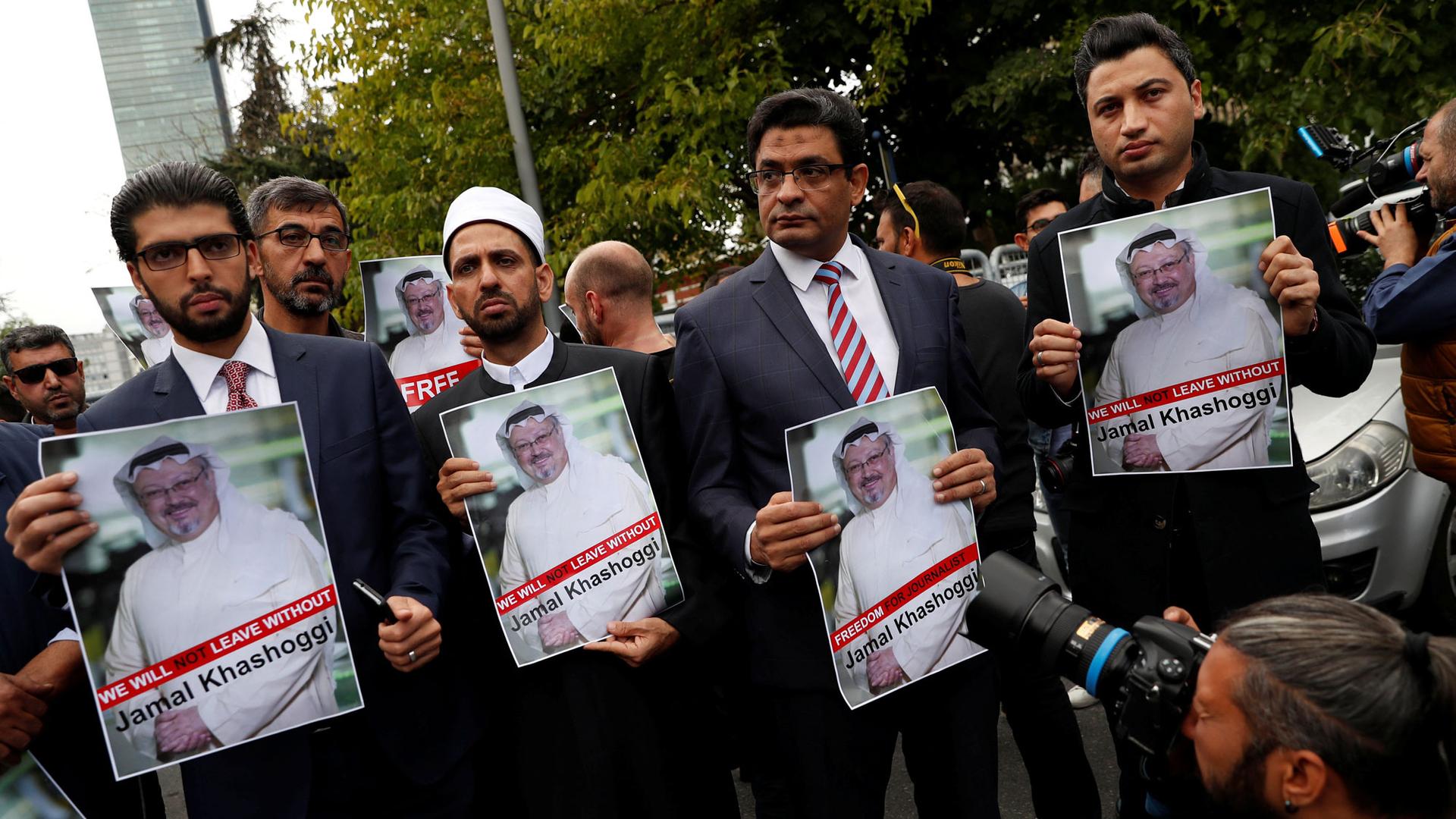Four men wearing suits stand abreast holding posters of Saudi journalist Jamal Khashoggi's picture.