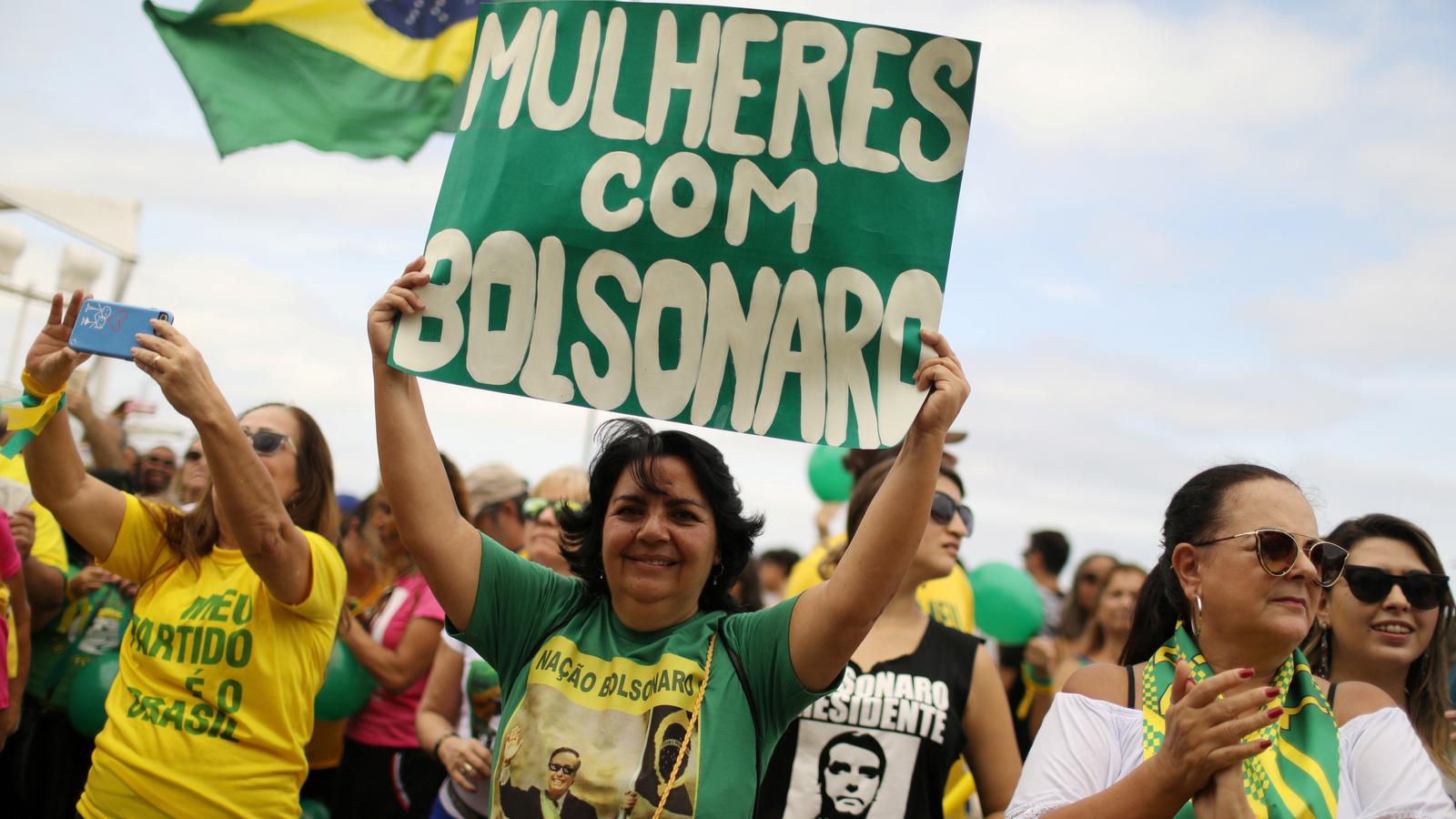 A woman holds up a green sign with white letters that says "Women for Bolsonaro" 