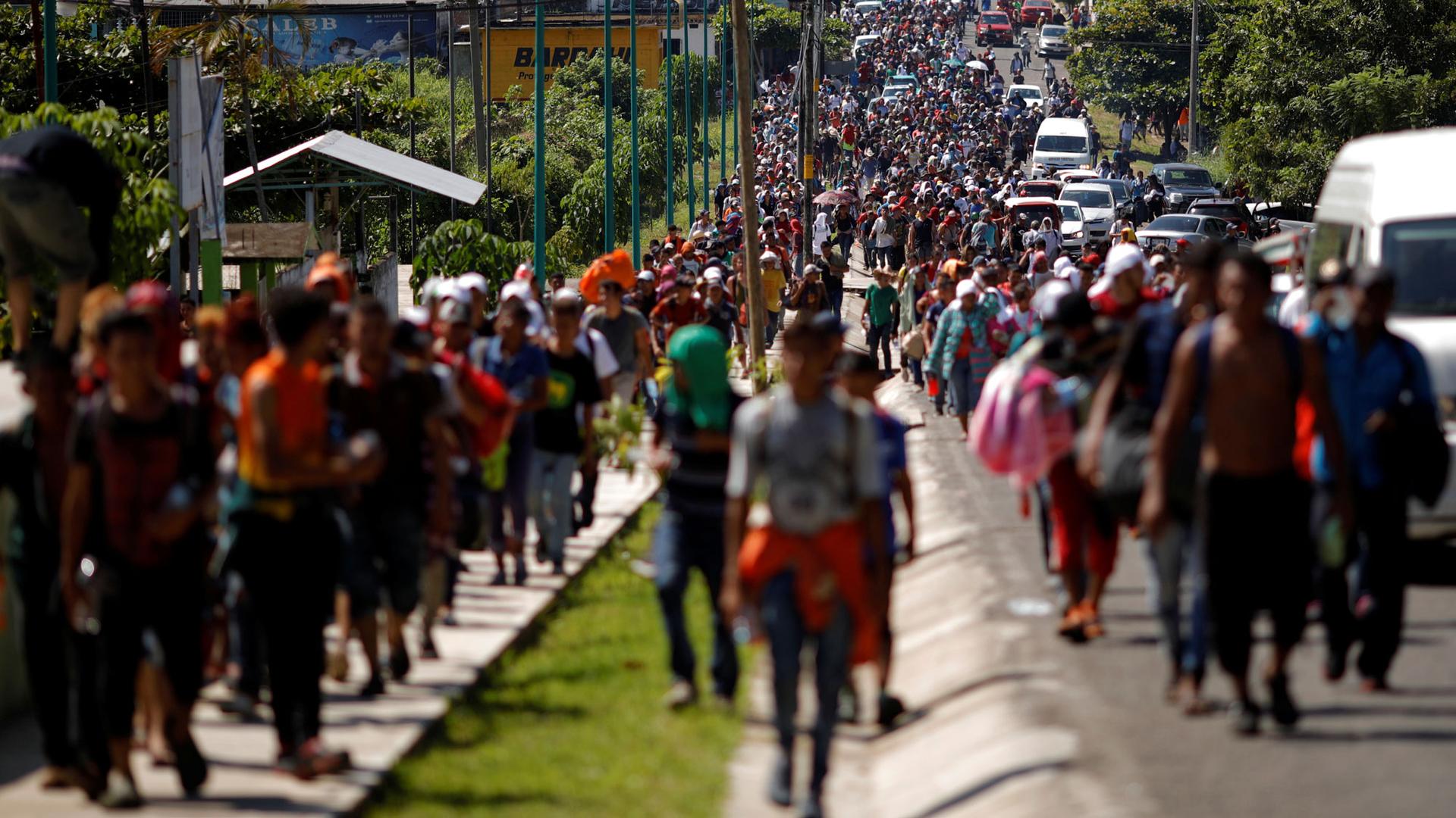 Central American migrants are shown walking on a road and sidewalk spreading the length of the highway in frame near the border with Guatemala.