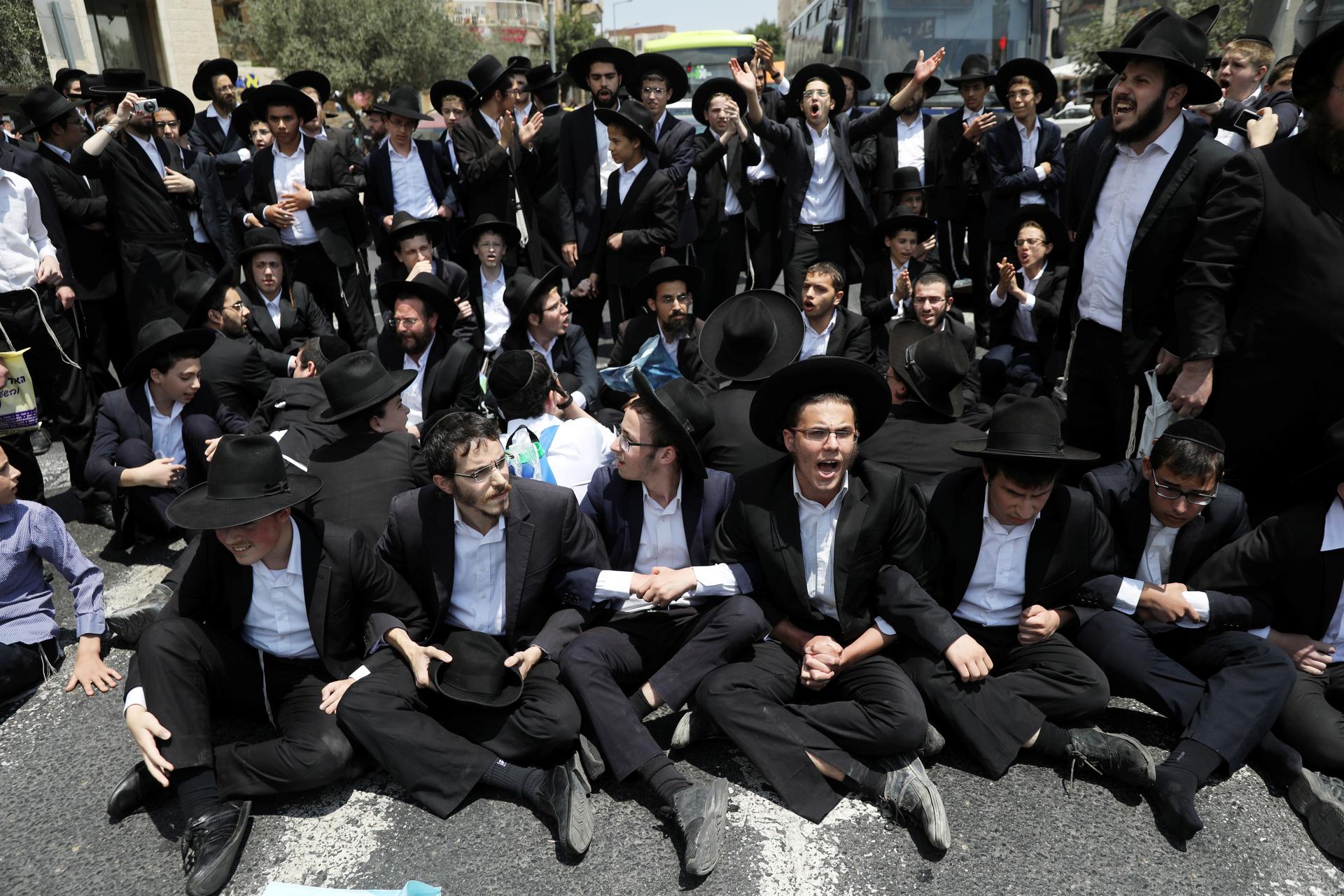 many Ultra-Orthodox Jewish men sit on the ground, linking arms