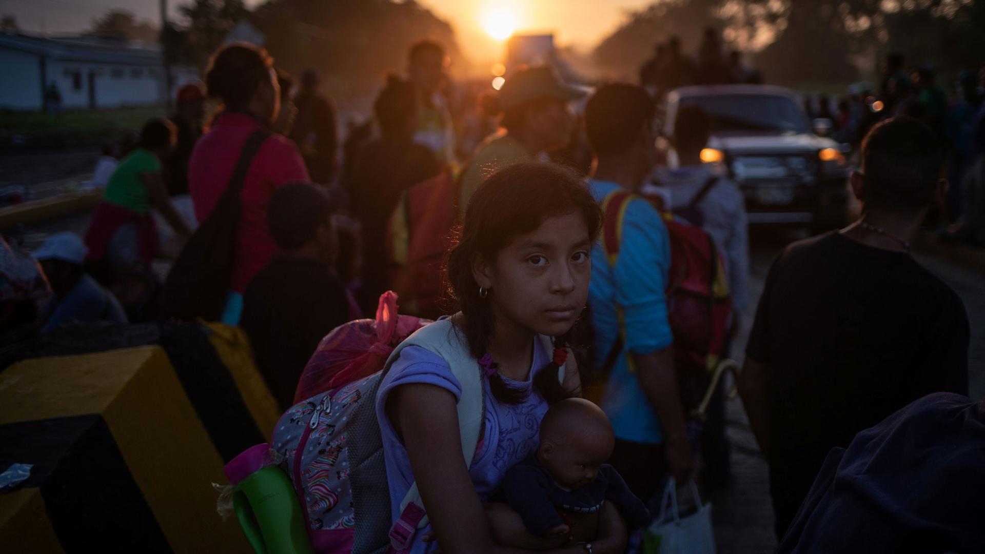 A girl traveling with other migrants is shown holding a doll and wearing a back-pack en route to the United States. 