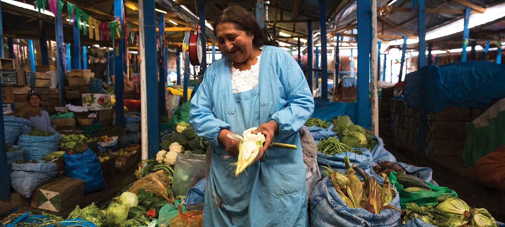 A woman wearing blue stands at her stall in the market