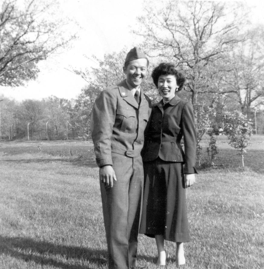 A black and white photo of a man in Army fatigues standing next to a woman in a suit jacket and skirt.