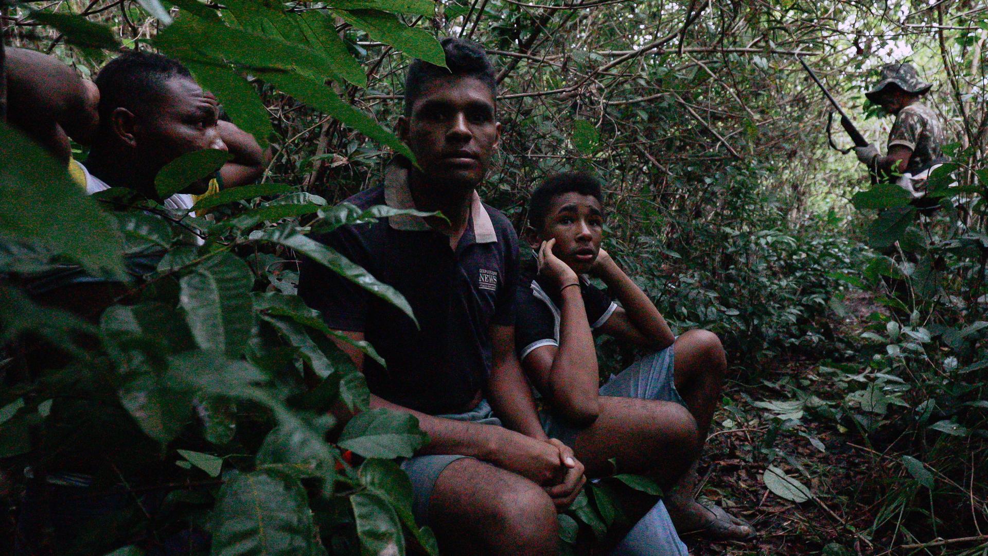 Three boys are on their knees in the jungle, with their hands clasped behind their heads.