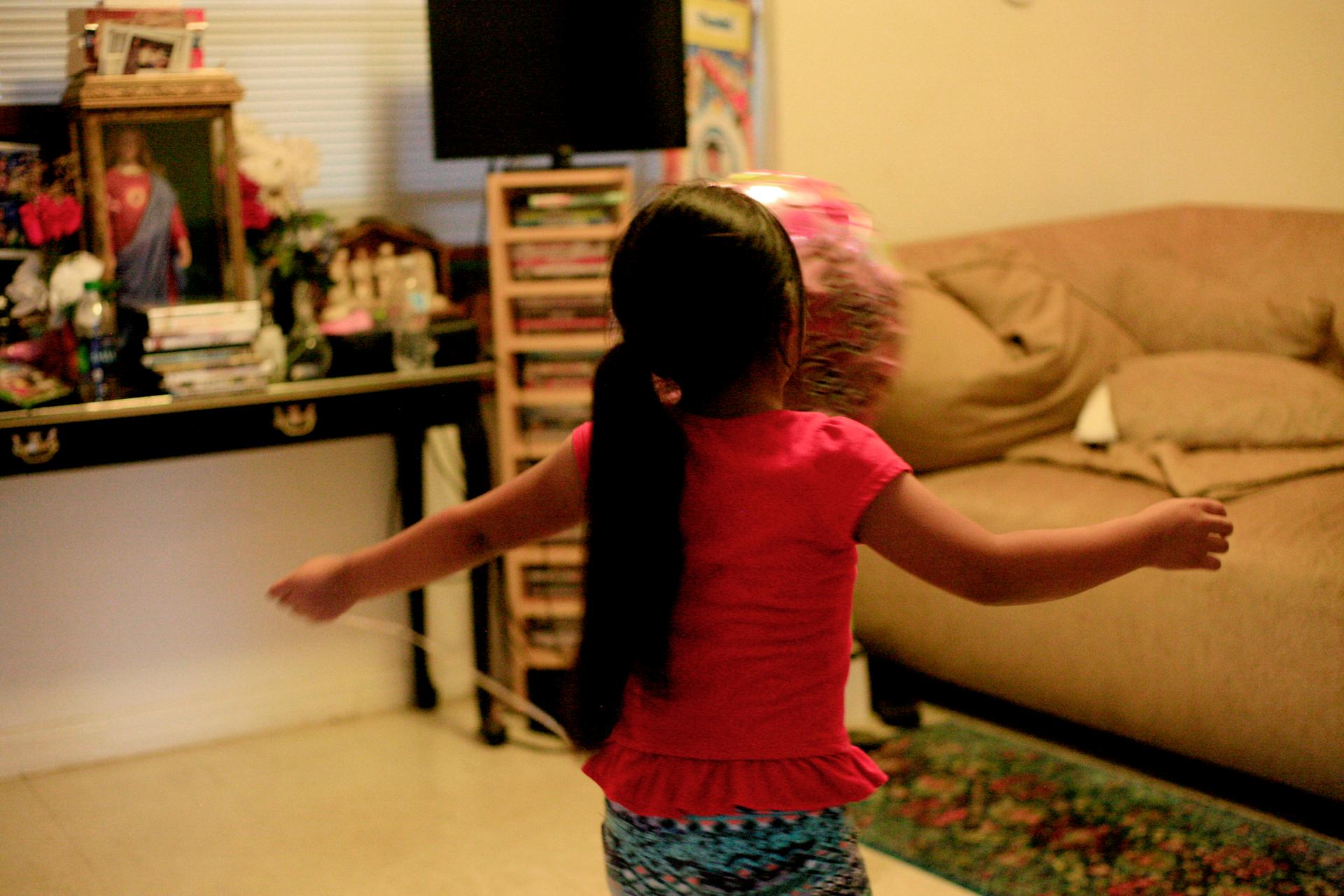 Young girl, shown from behind, with arms outstreched, in room in home
