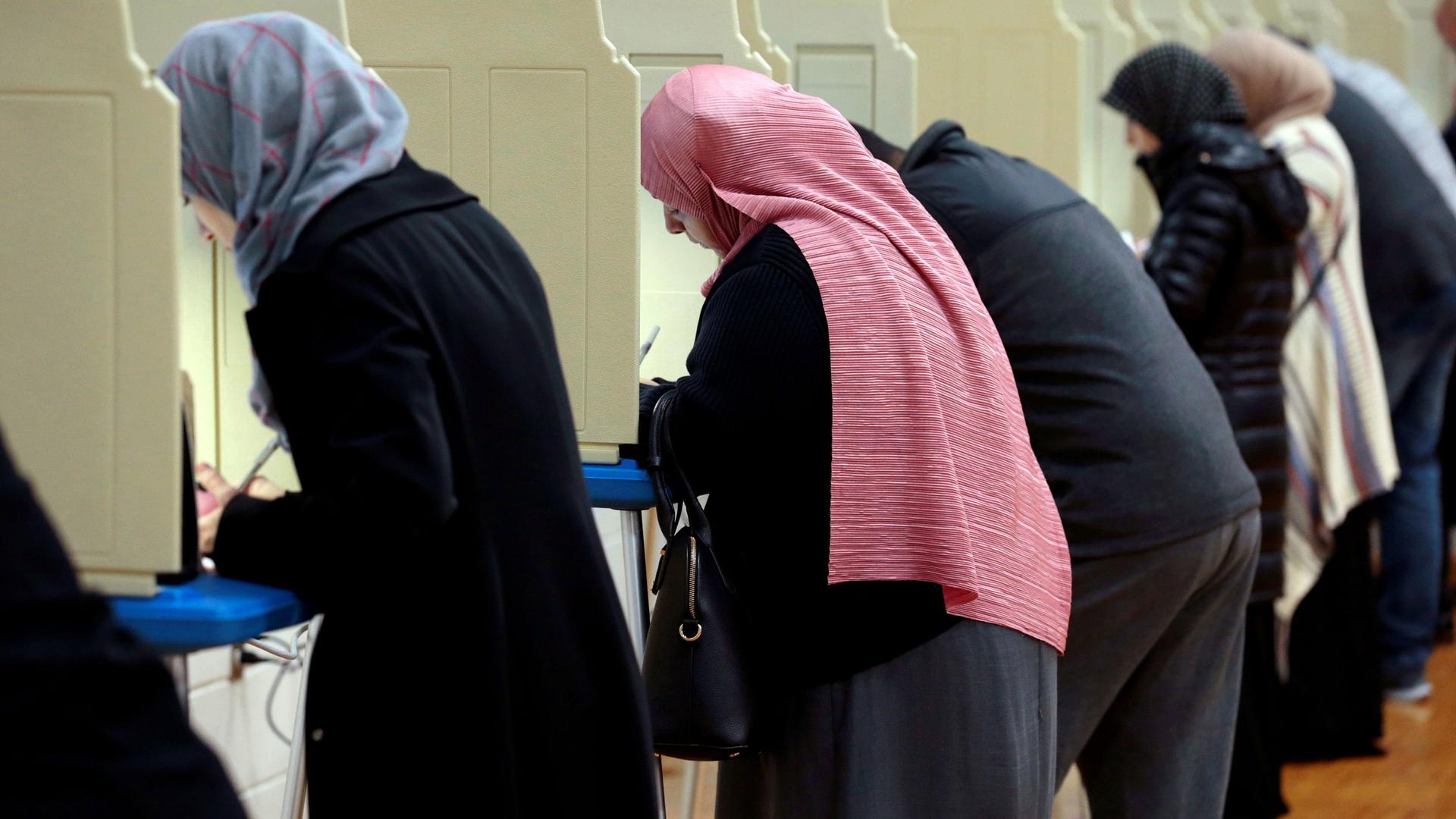 Women wearing headscarves cast ballots in a line of voting booths.