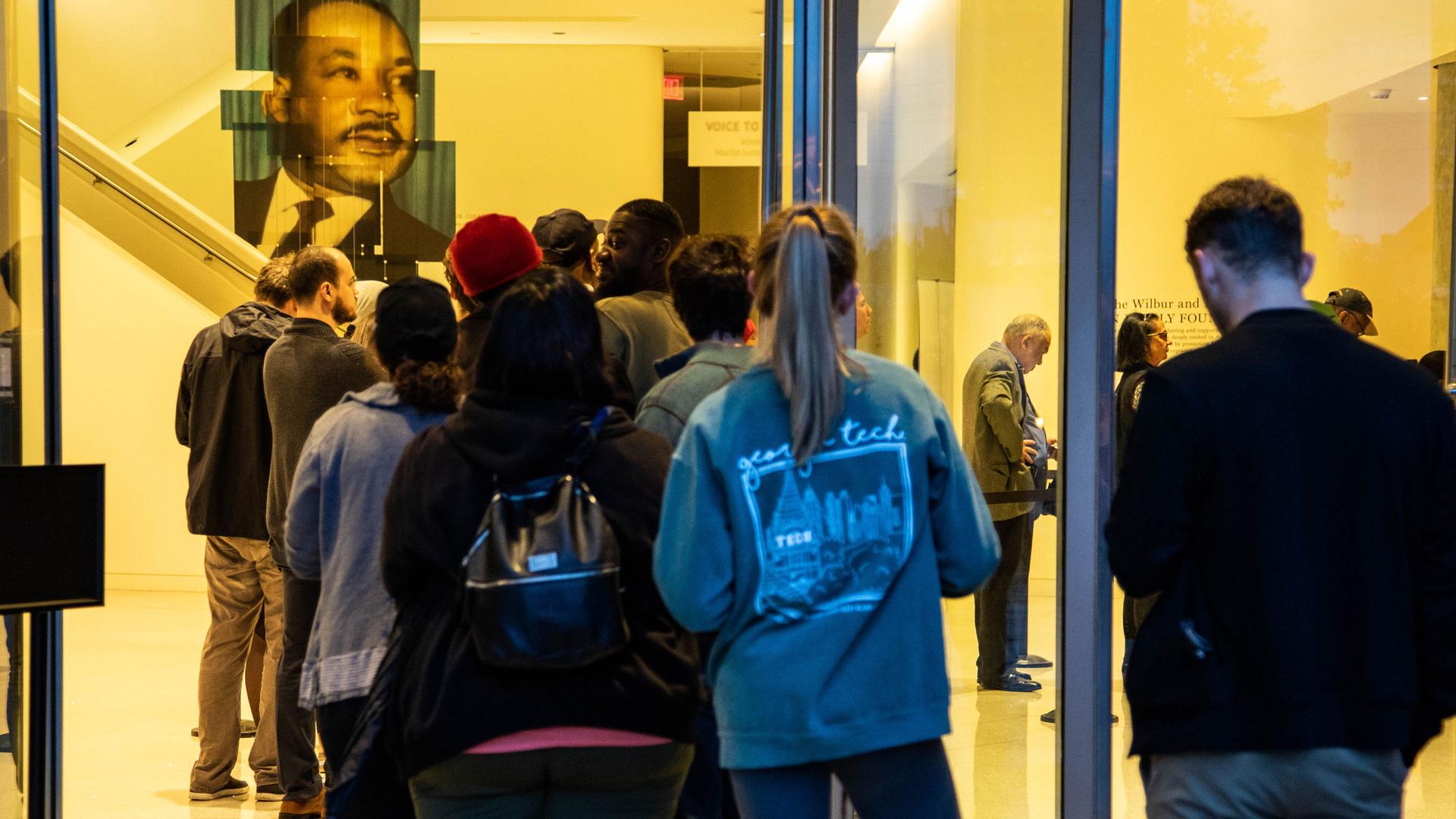 People line up in a voting queue. Above them is a portrait of Martin Luther King Jr.
