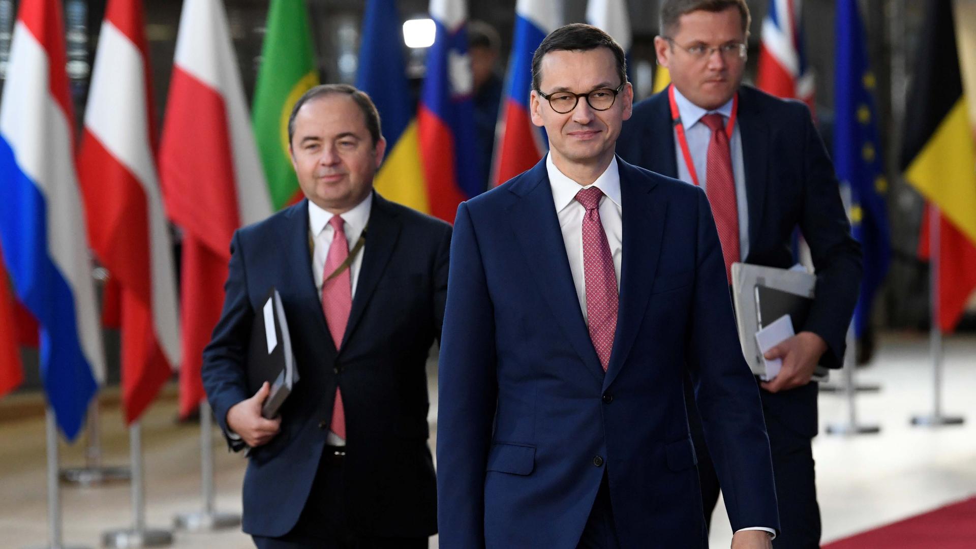 Three men in suits walking in front of flags